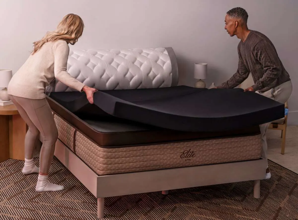 Two people adjust a foam mattress topper on a bed.