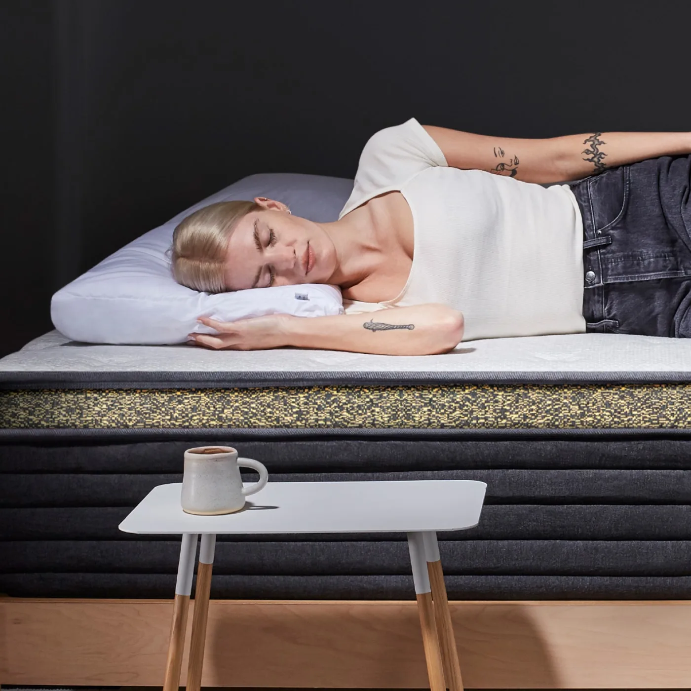 A woman sleeps on a mattress, with a mug on a side table.