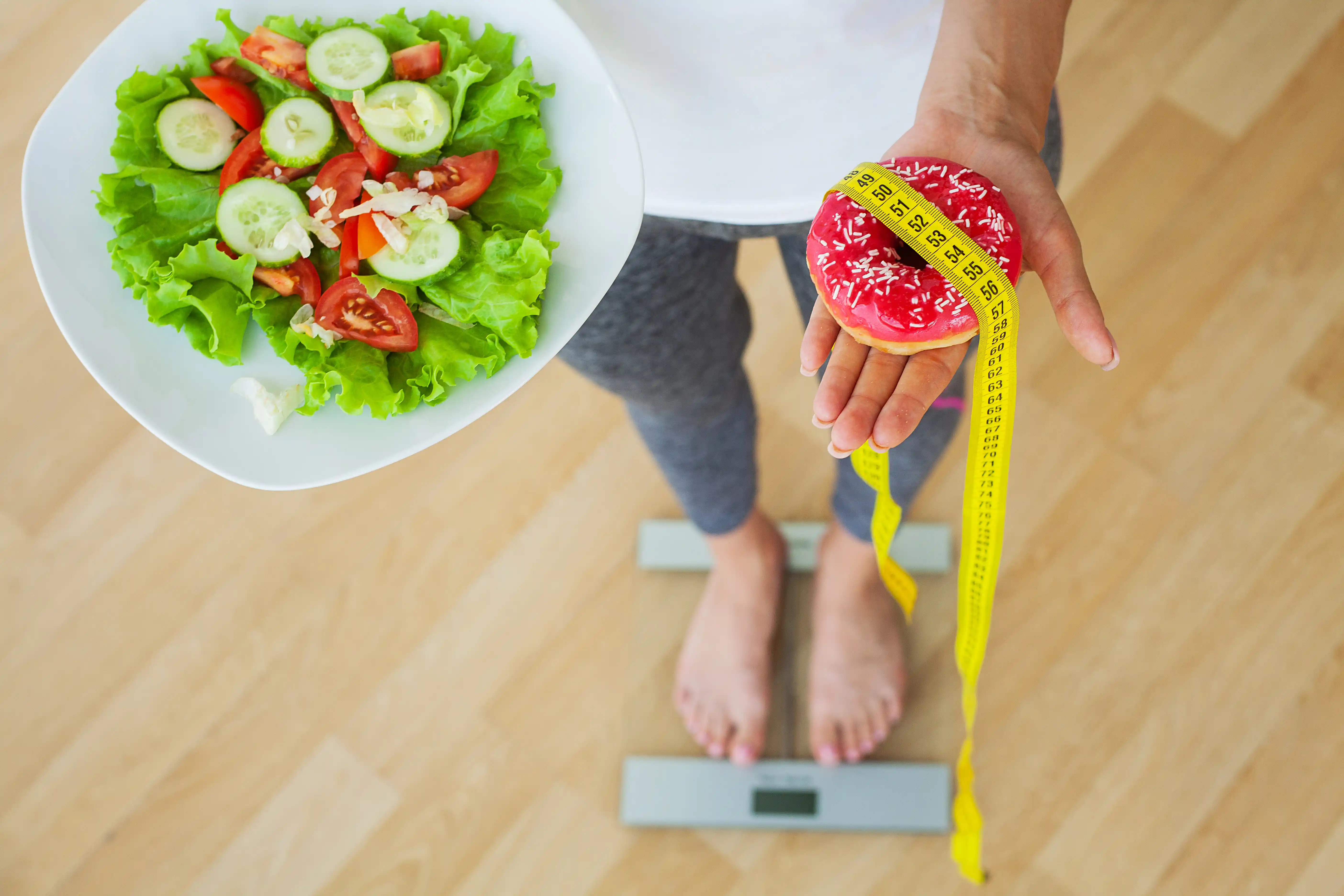 Diet concept, woman measures weight on electronic scales while holding calorie donut