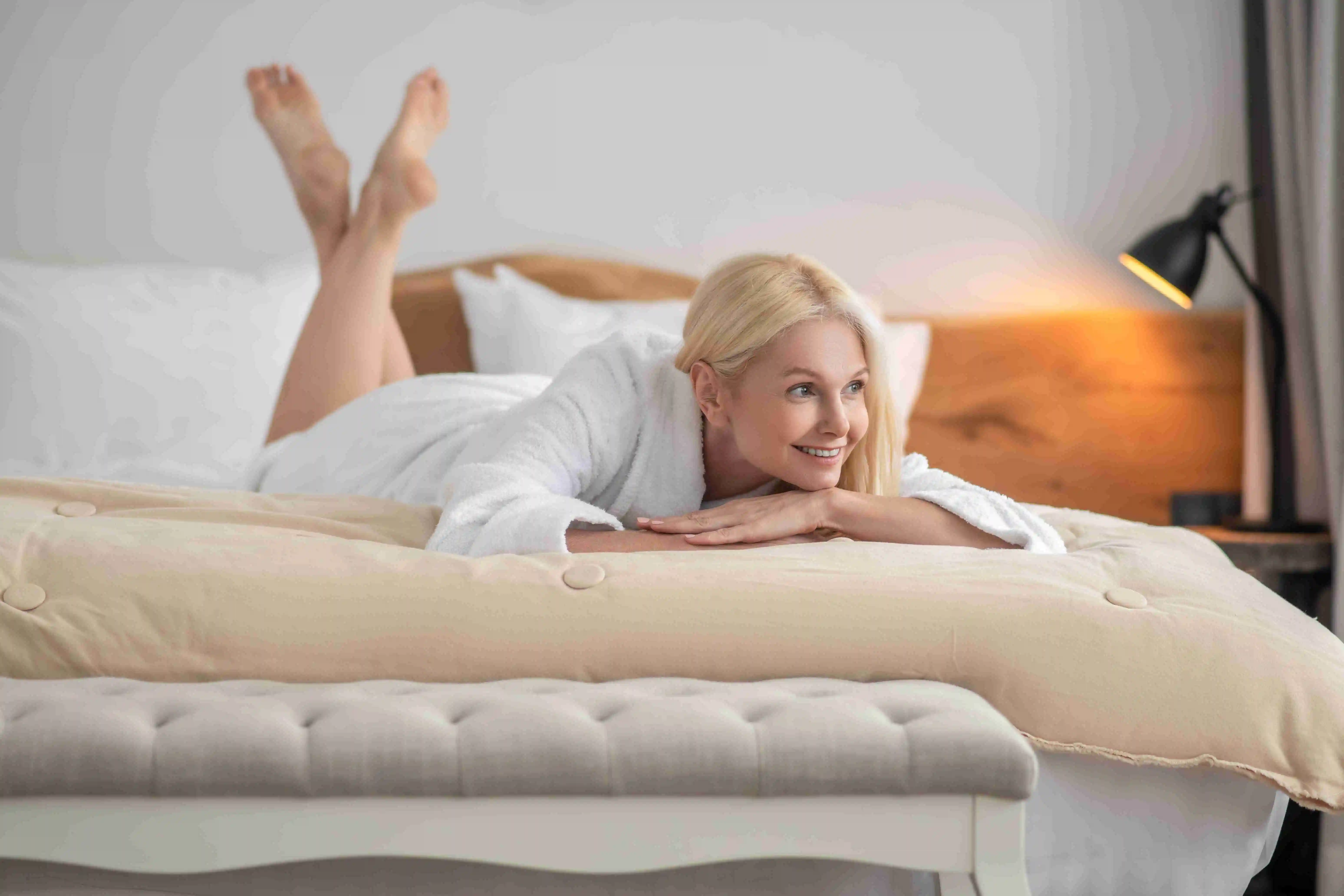 A beautiful woman in a white bath robe laying on a mattress topper