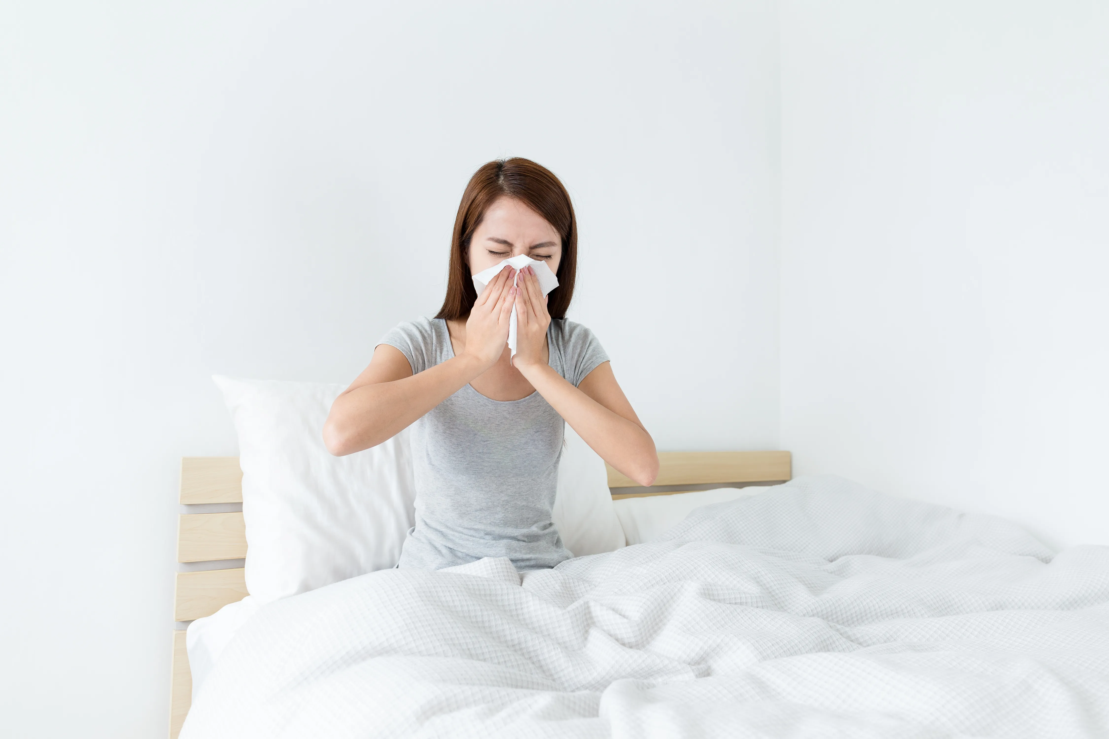 A woman sneezing while sitting on a bed