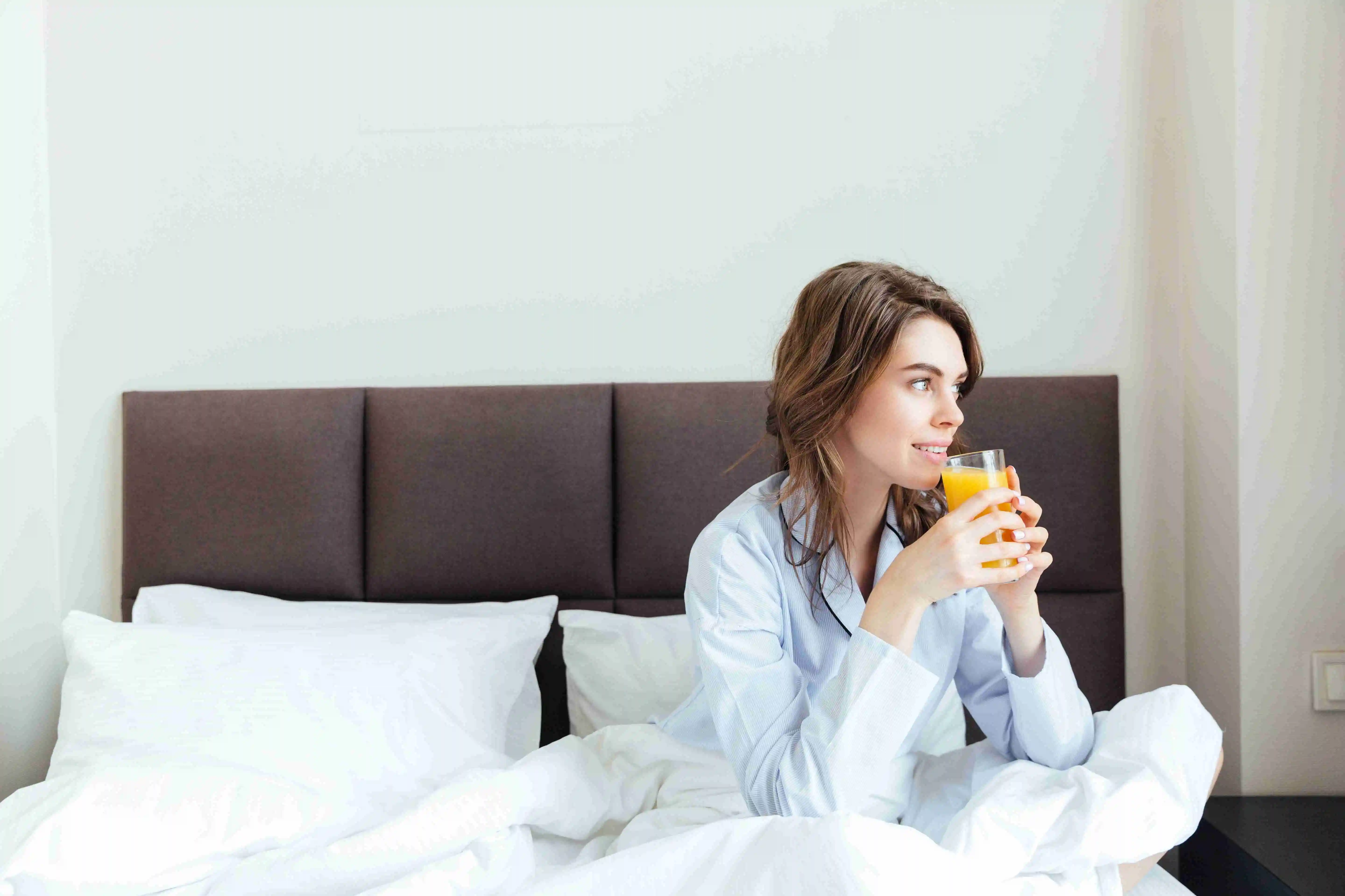 Portrait of a beautiful woman drinking orange juice in bedroom