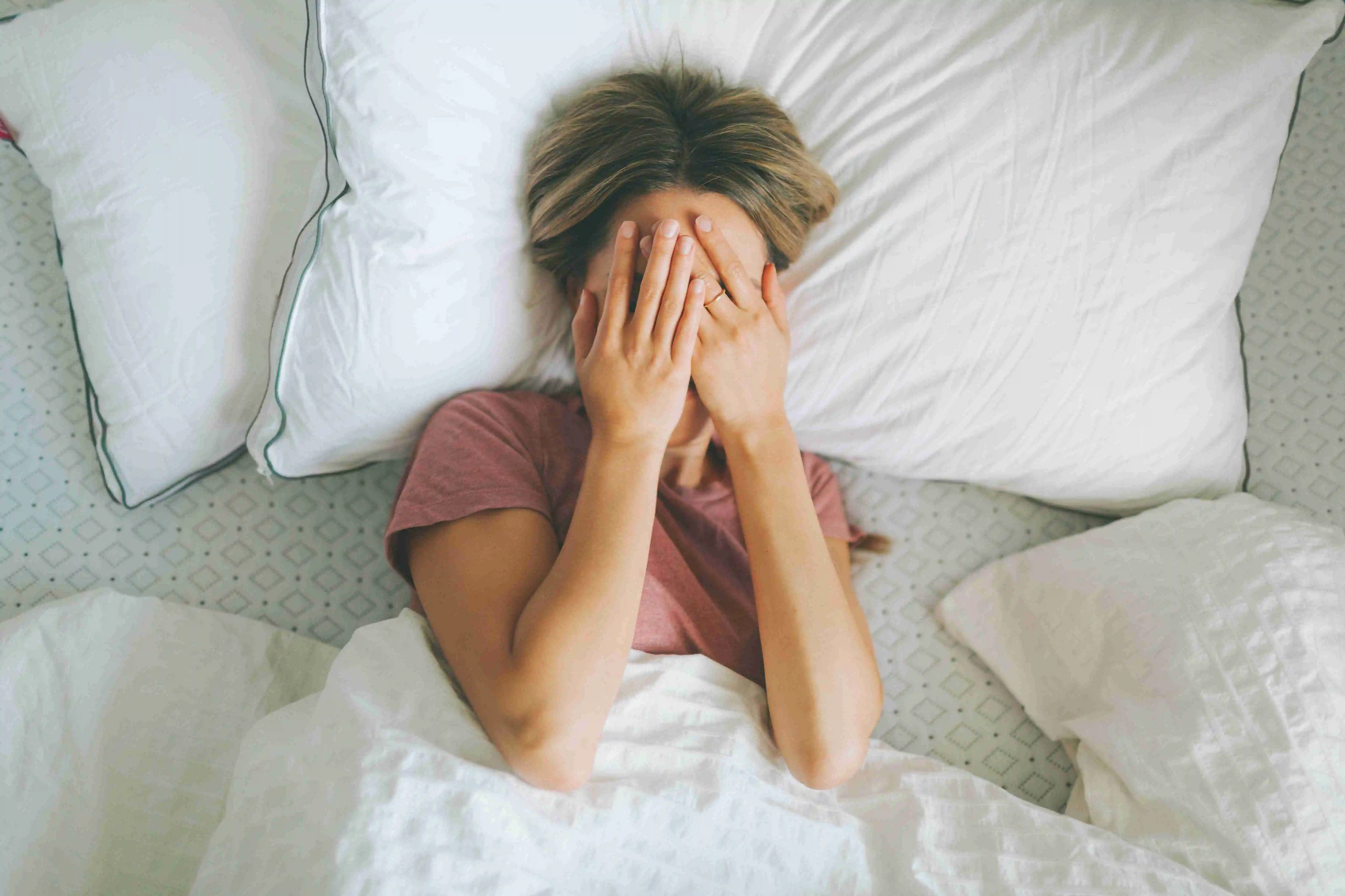 A woman covering her eyes with her hands, wanting to stay in bed.