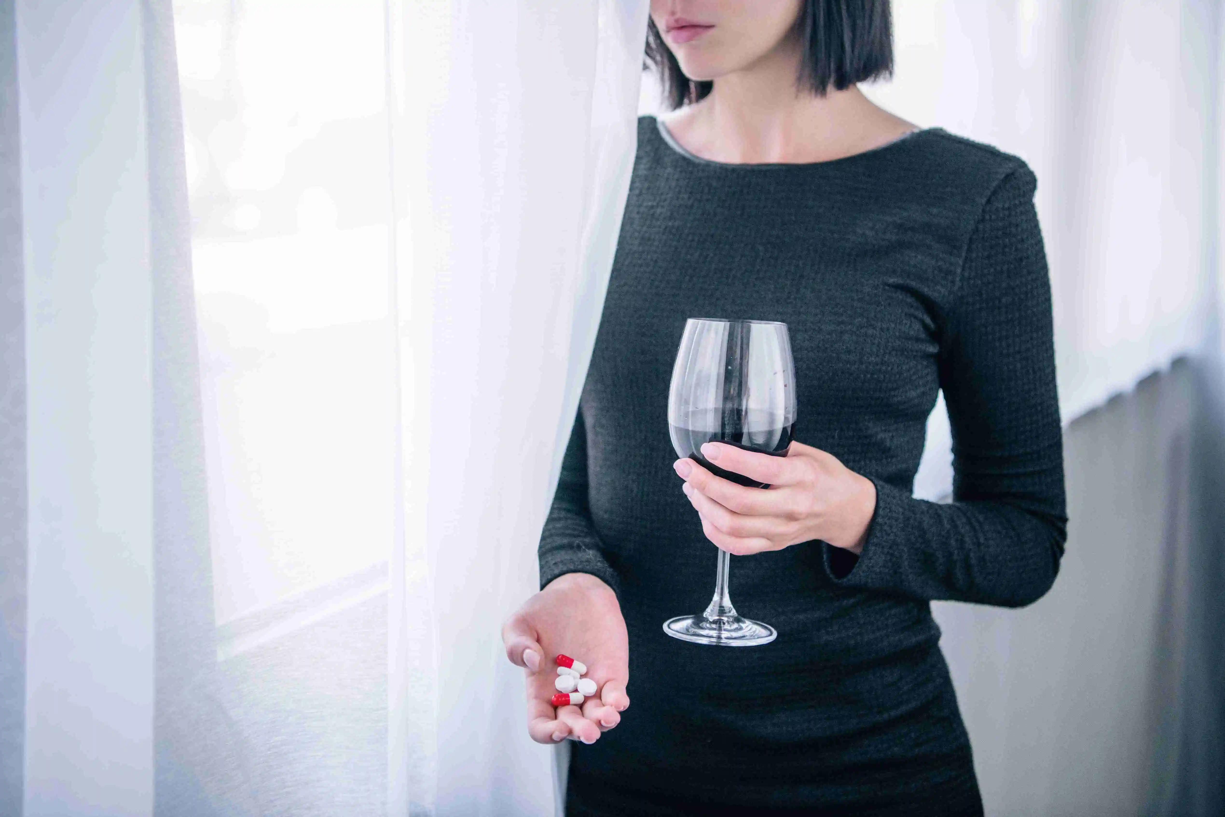 Cropped view of depressed woman with wine glass and pills at home