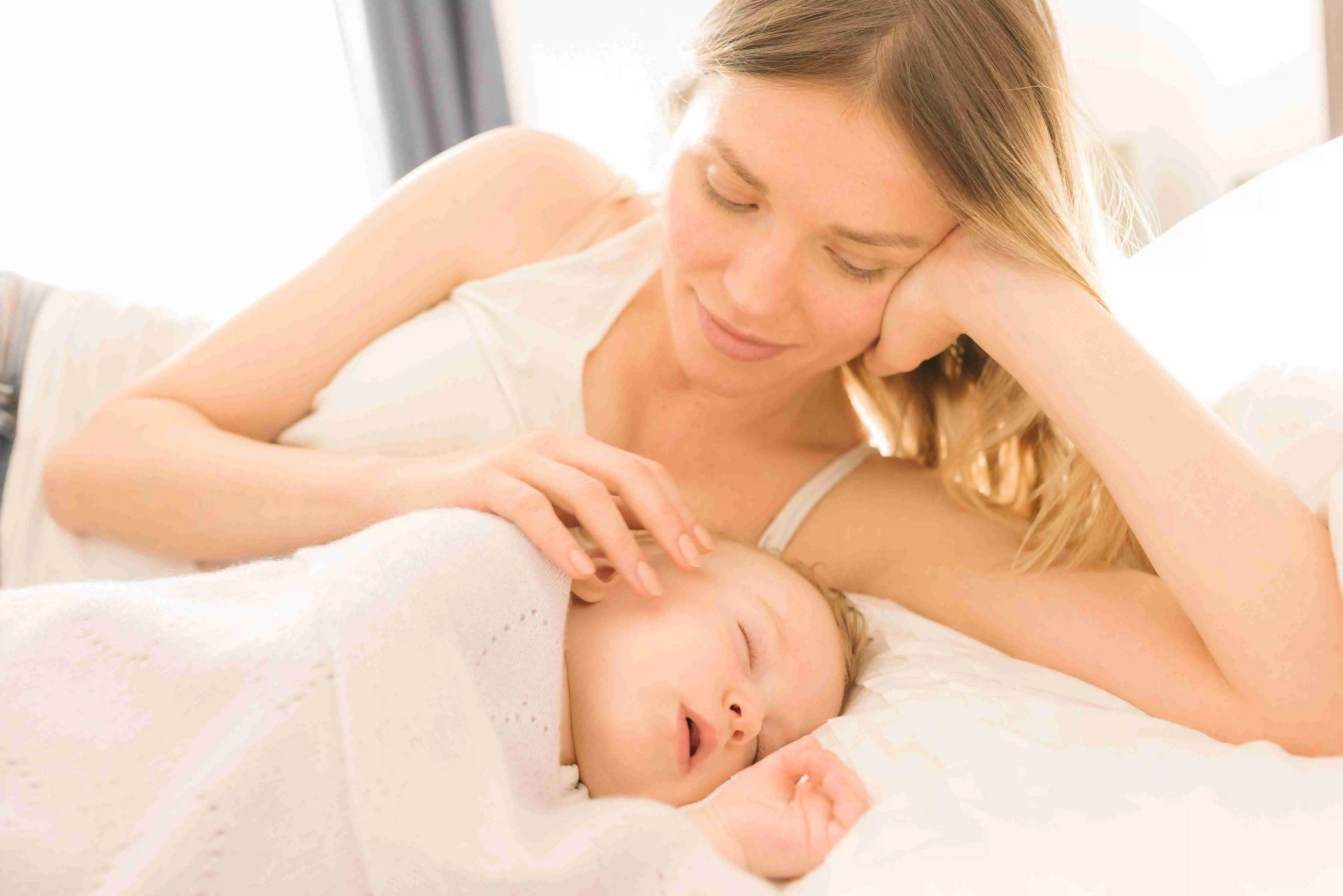 Mother watching over sleeping baby on bed