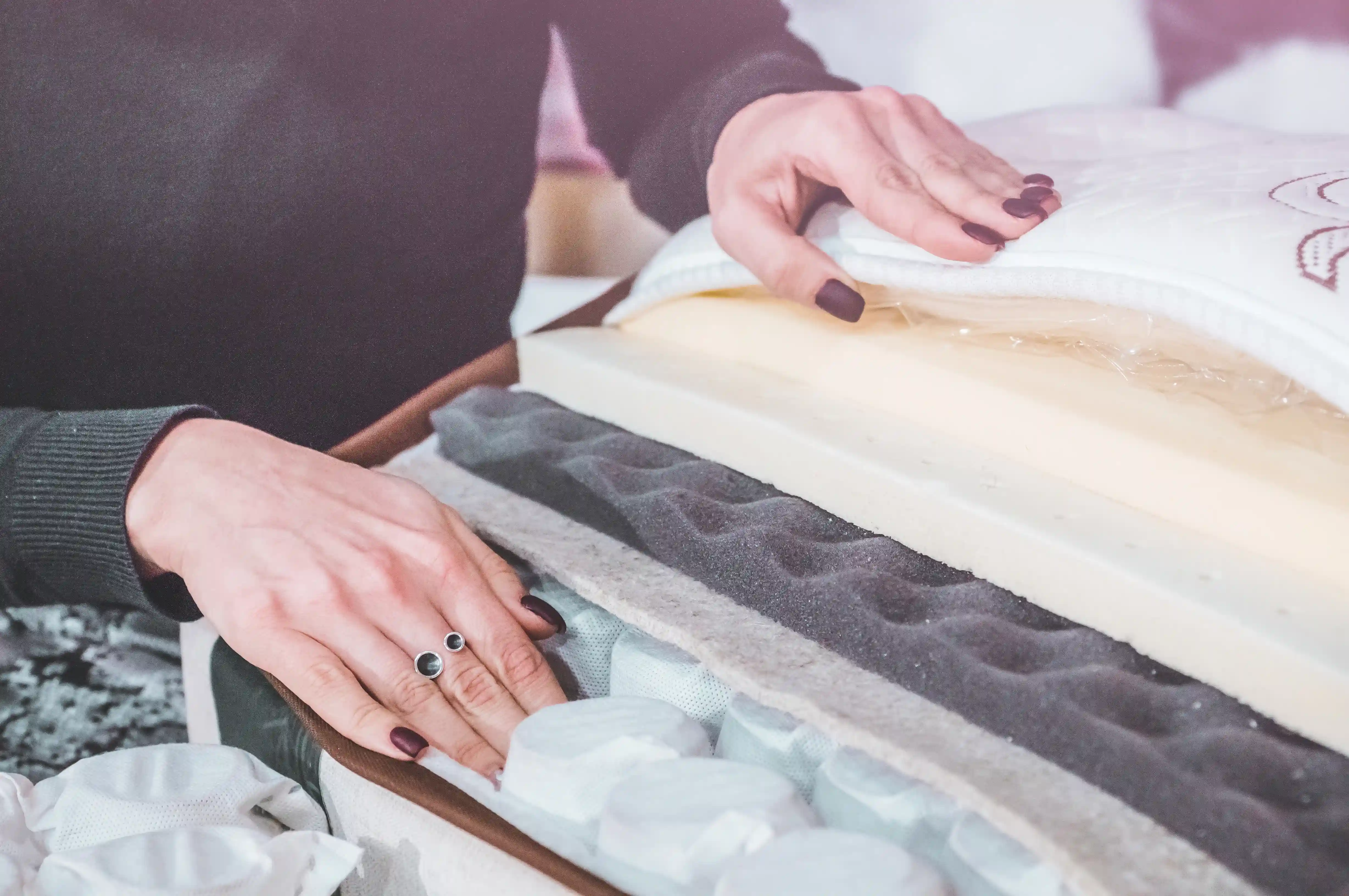 A reviewer's hands testing the layers of a hybrid mattress  