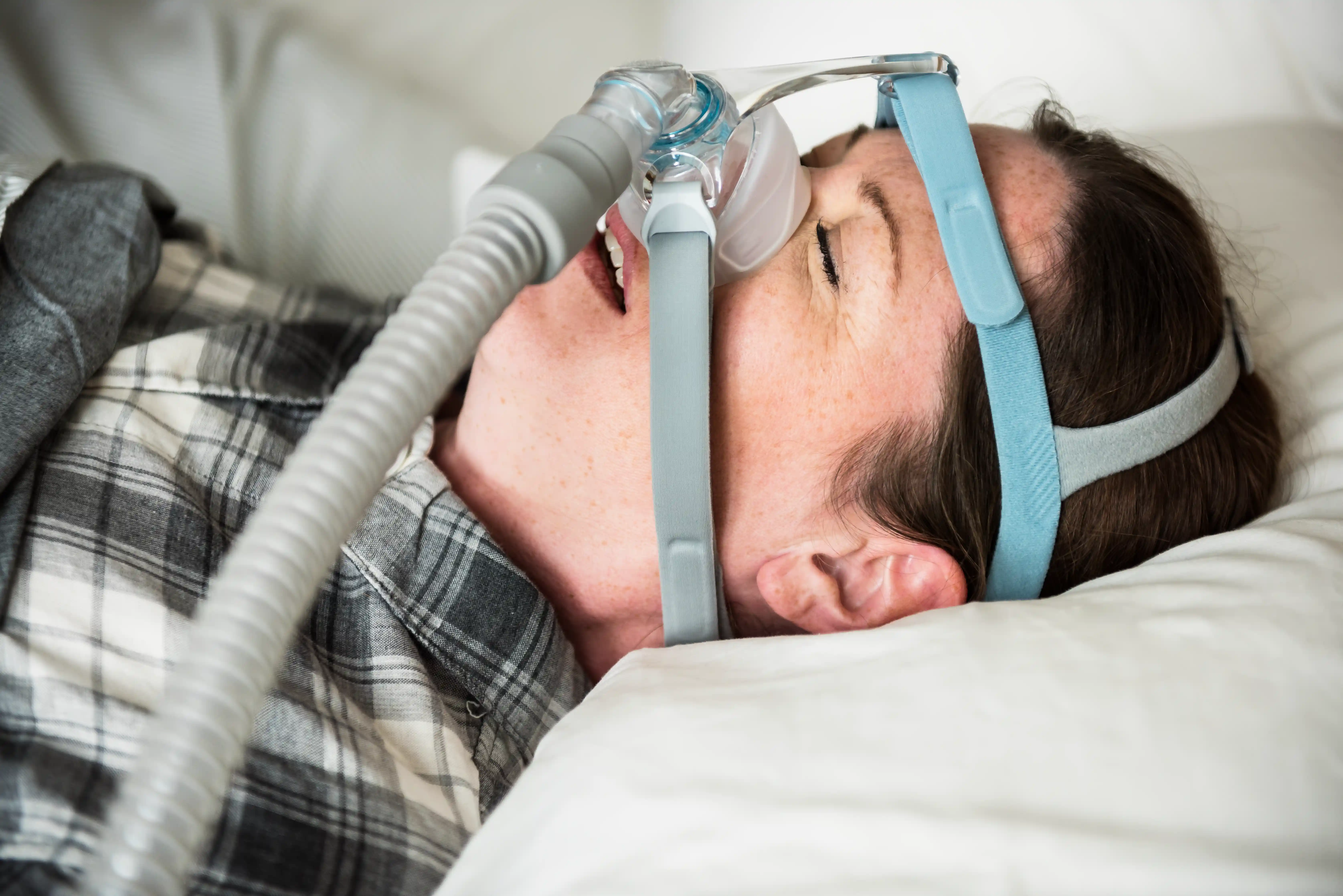 Adult resting in bed wearing a nasal PAP mask connected to tubing, illustrating the benefits of adaptive servo-ventilation (ASV) for sleep apnea