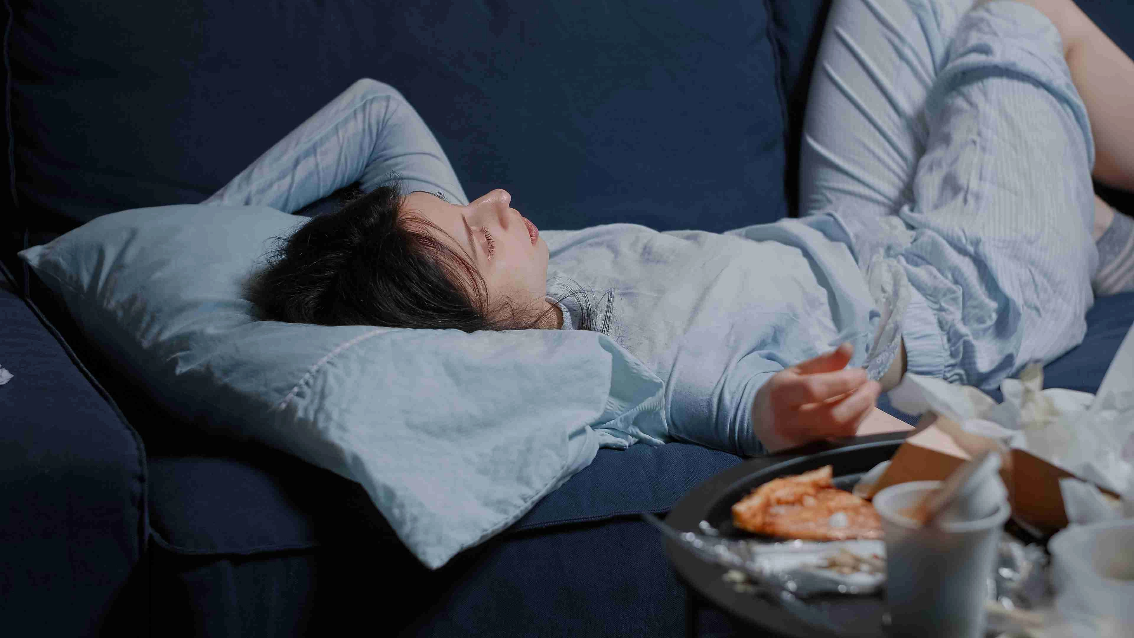 woman lying on sofa looking lost at messy table