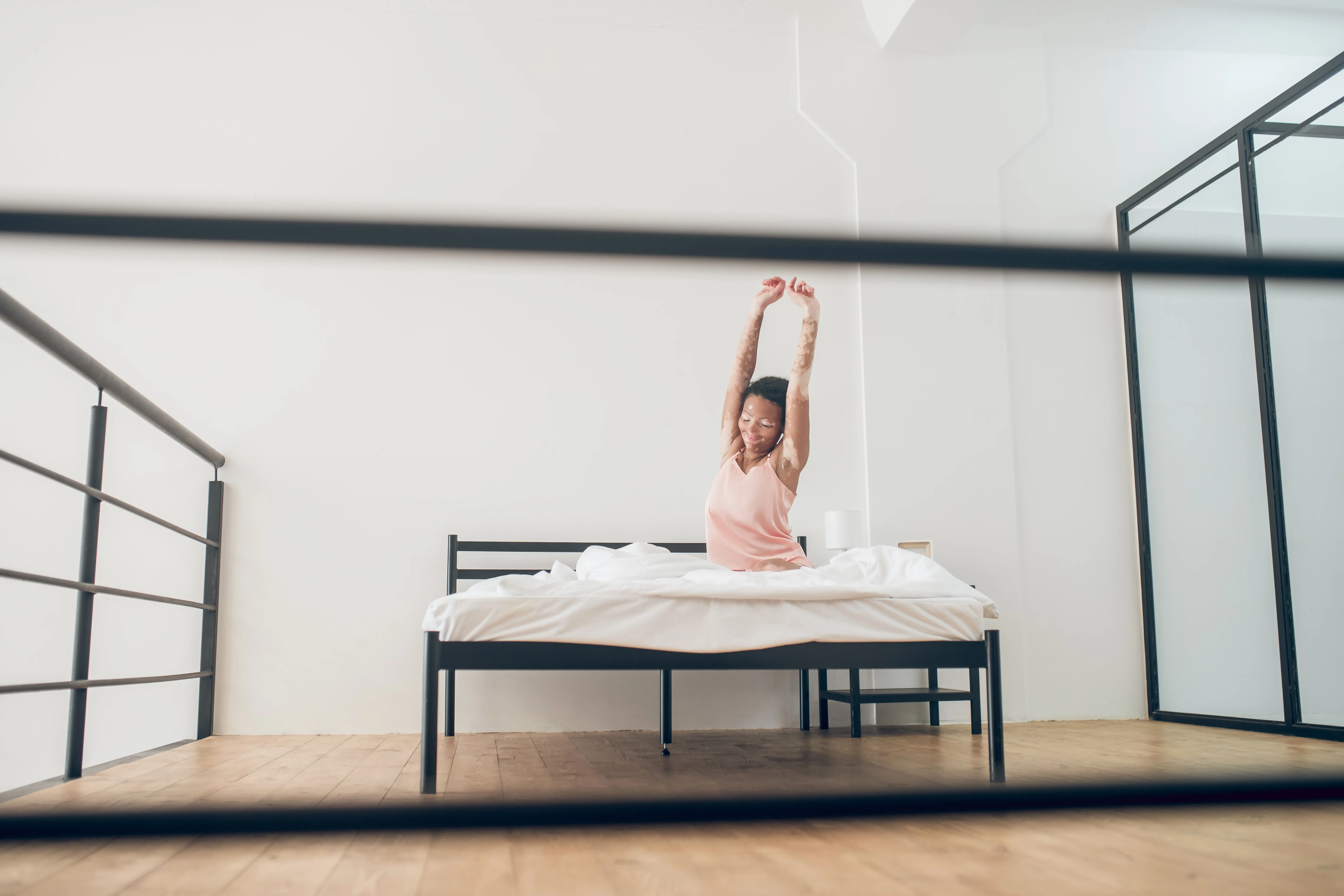 A person stretching on a bed with a metal box spring, in a bright room.