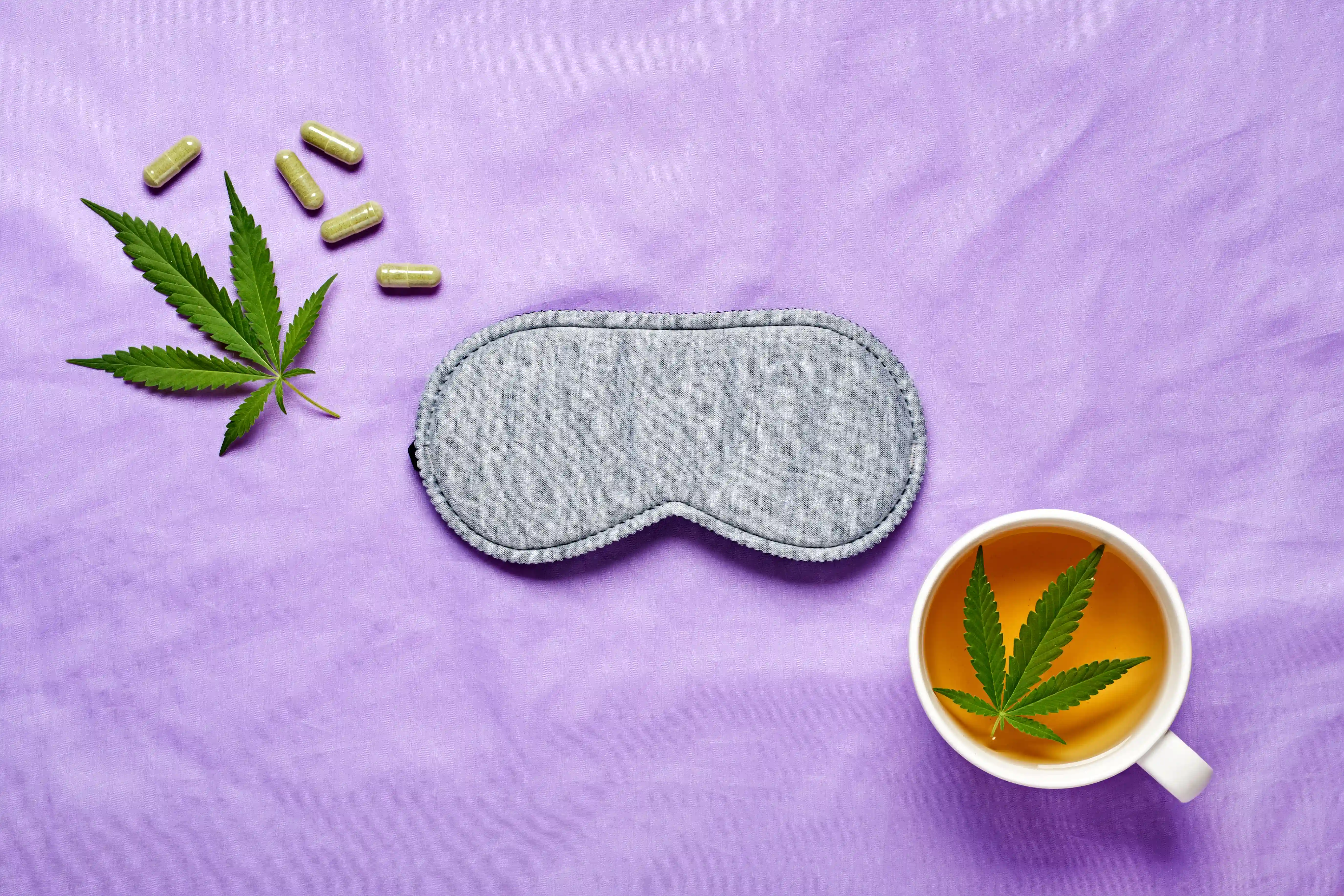 Healthy night sleep concept. Sleep mask, calming hemp tea and hemp capsules on silk lilac background
