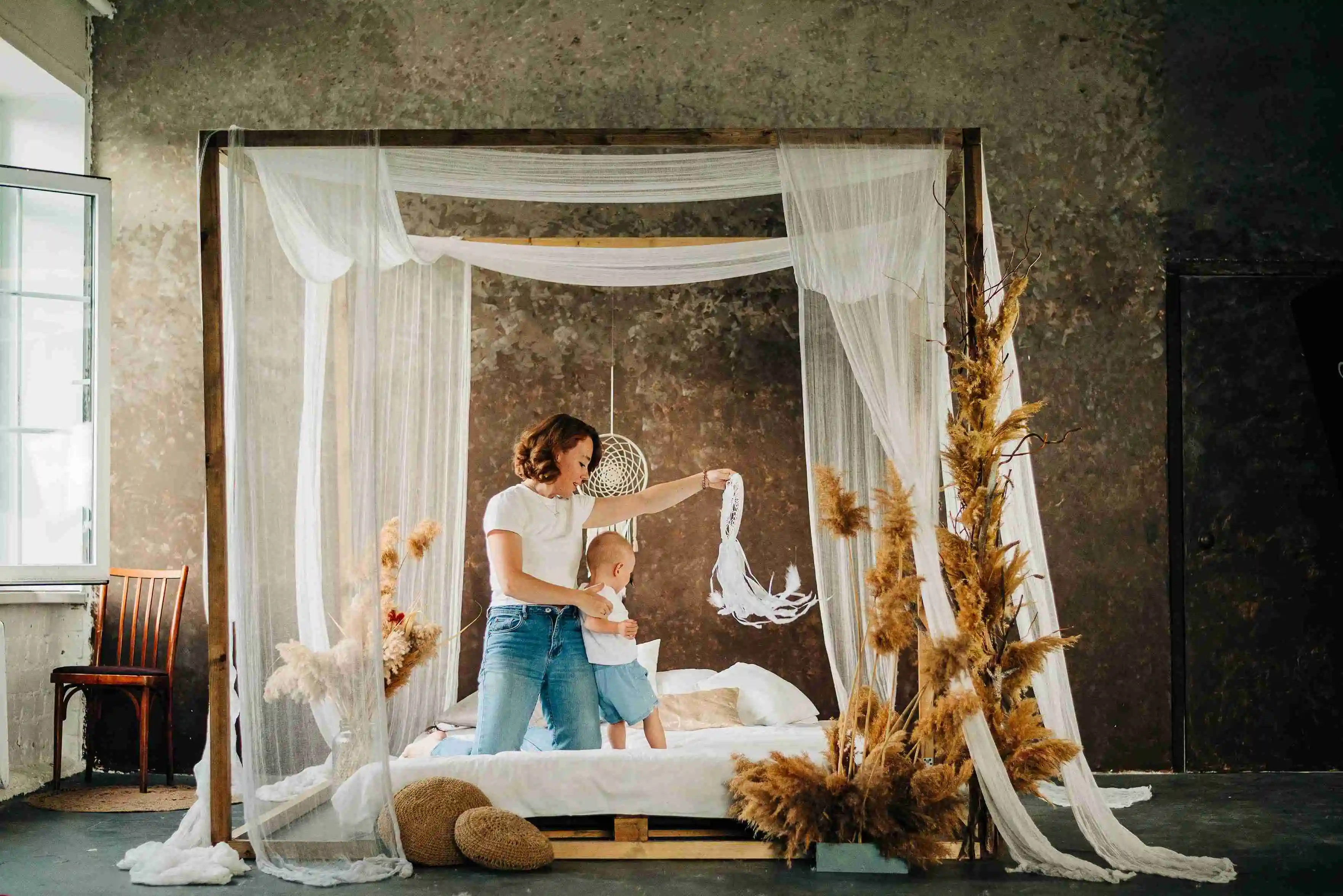 Mom and her baby daughter lying on the beautiful bed in boho style.