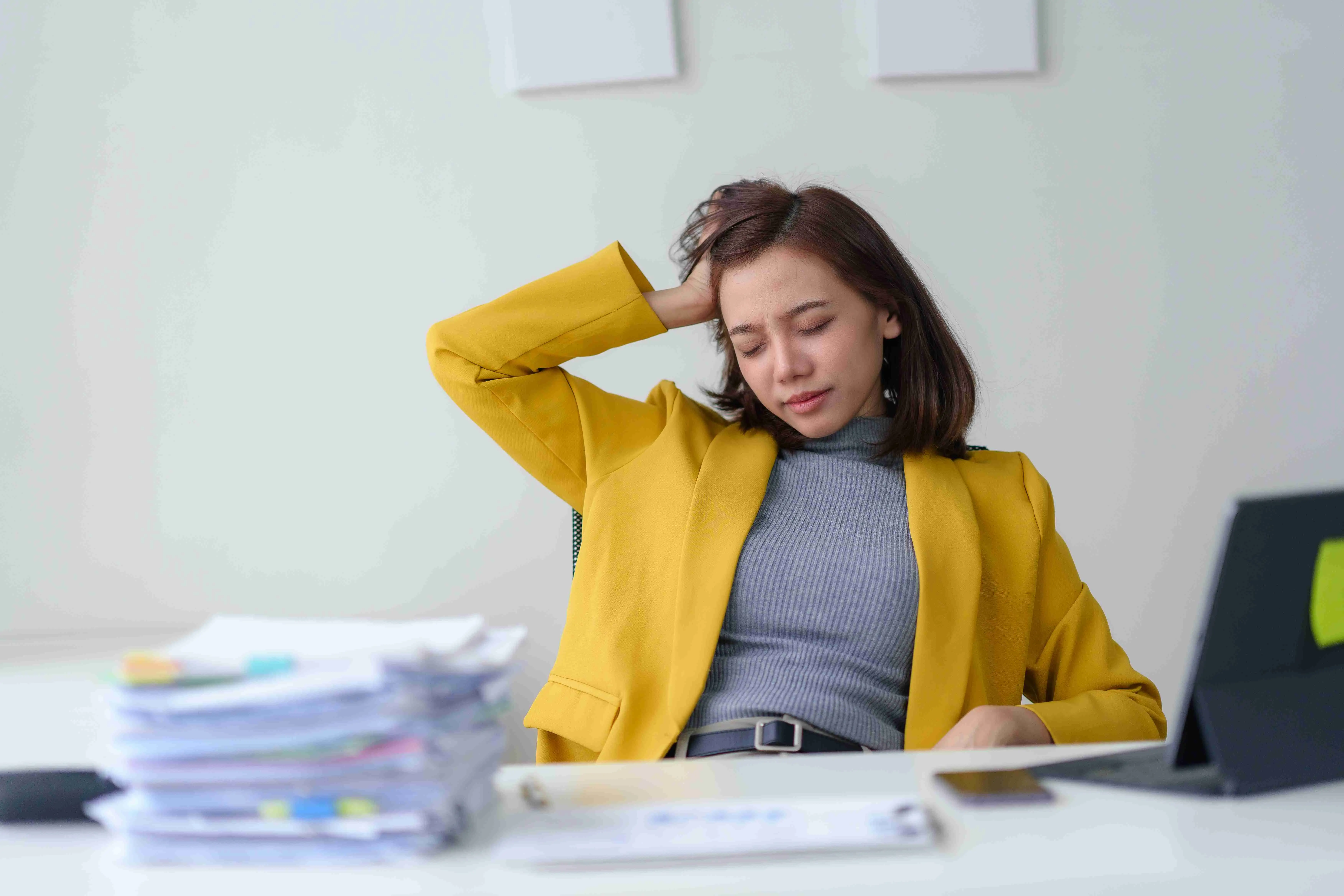 Young woman sitting at office desk, looking tired and stressed