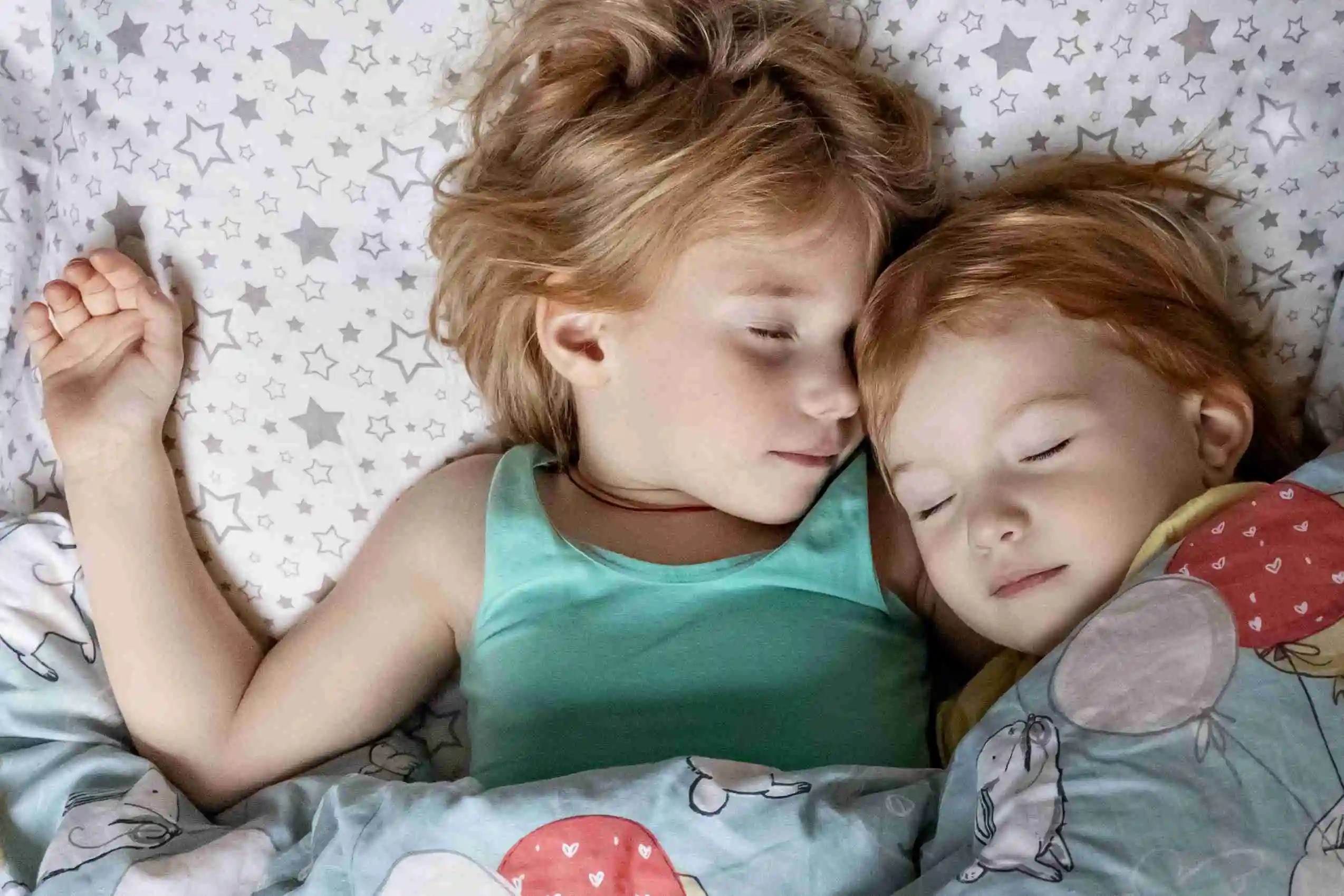 Two little girls, sisters sleeping in a bed under one blanket