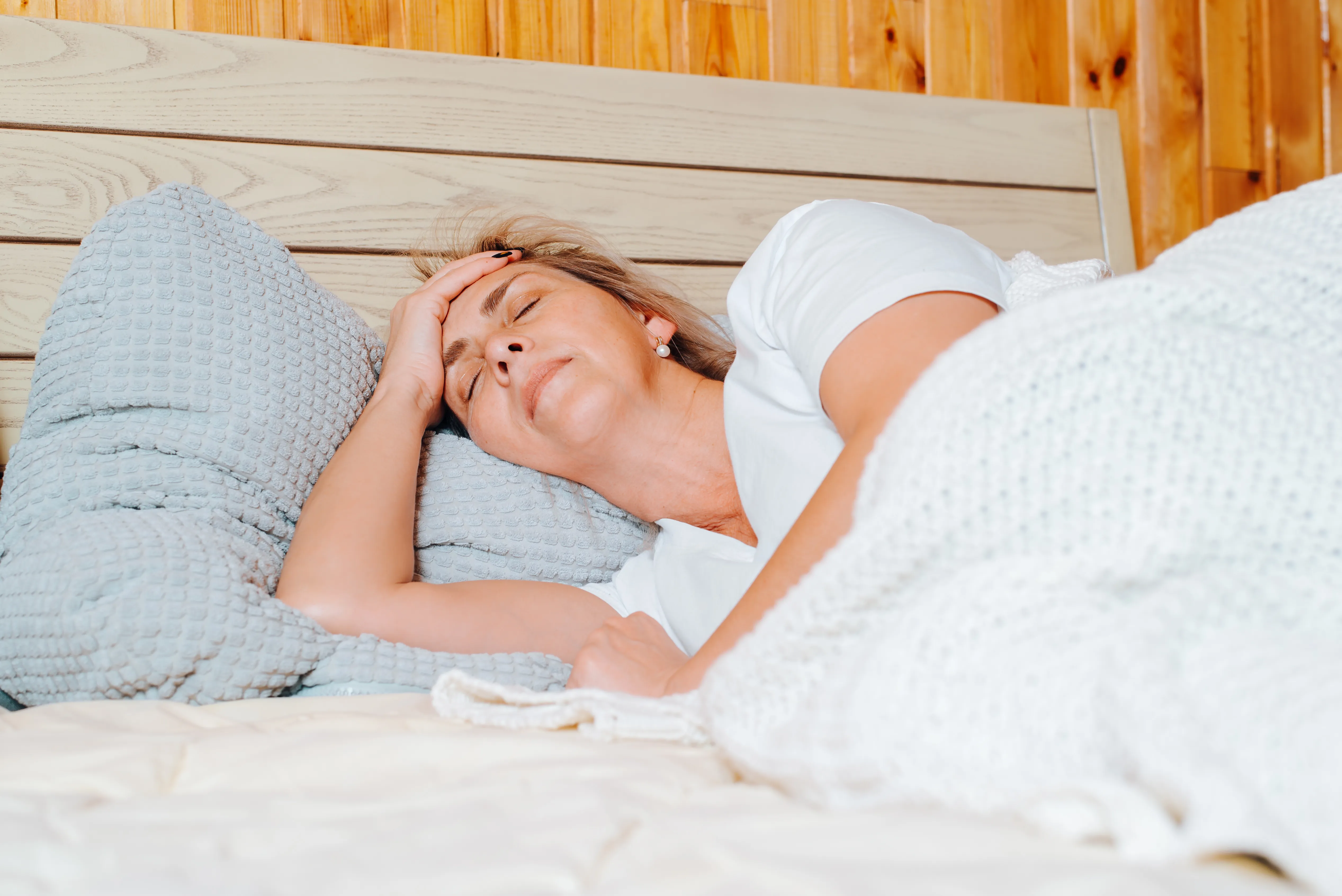 Adult caucasian woman with headache lying alone on bed in bedroom with closed eyes.