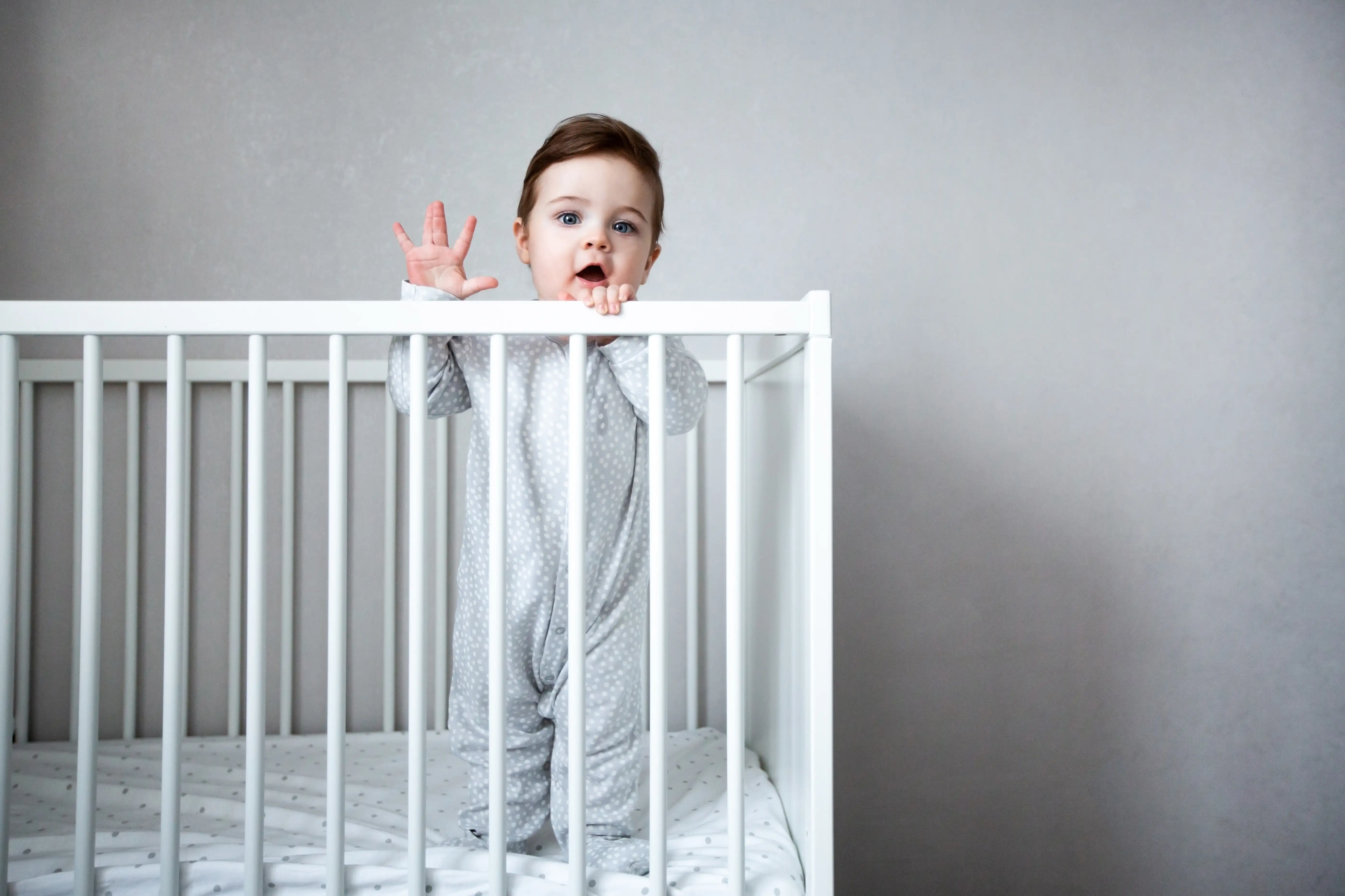 Awake baby standing in an empty white crib