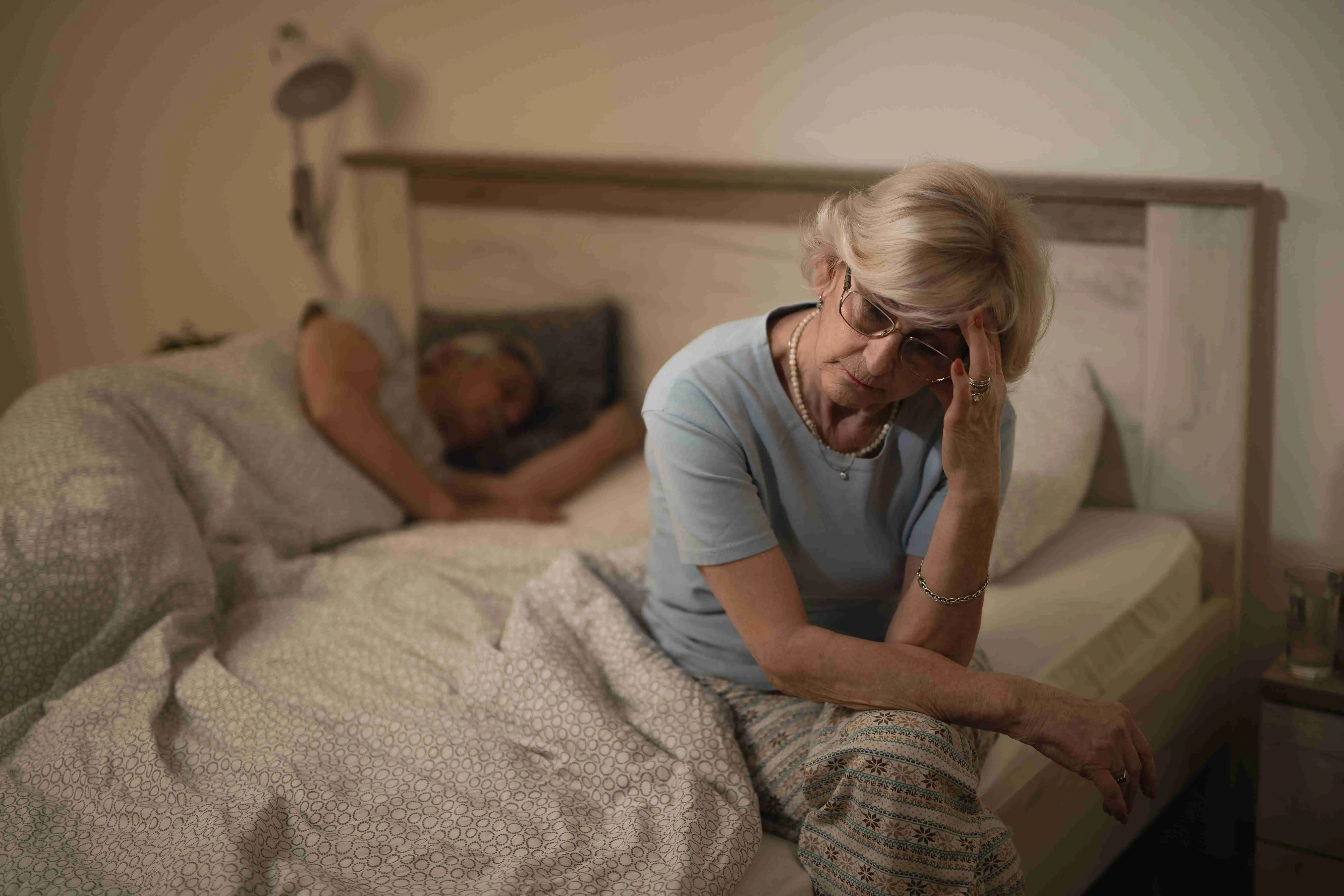 Sleepless senior woman siting on the bed at night.