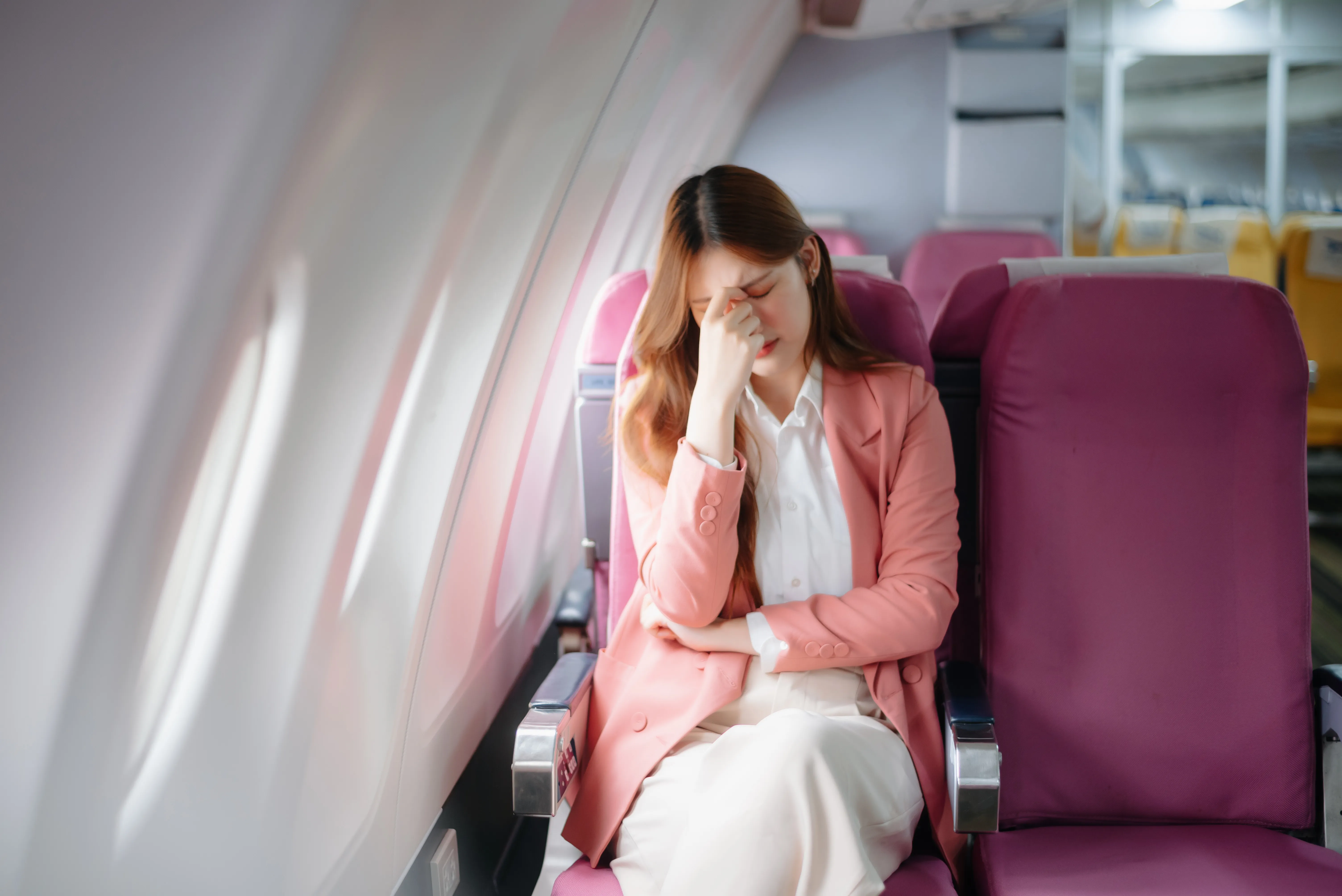 Photo of a frustrated woman sitting on an airplane with her head in her hands