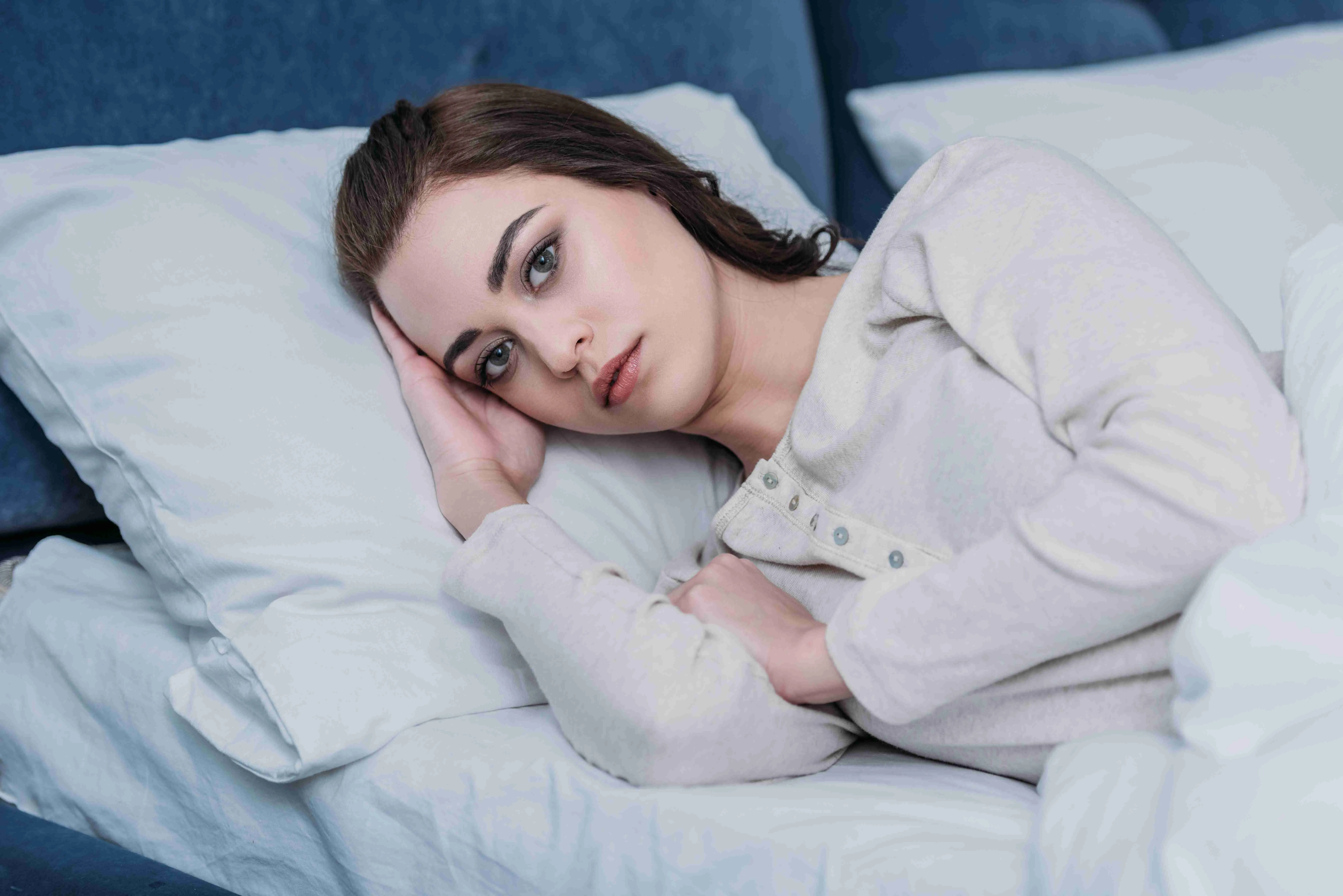 beautiful sad woman in pajamas lying in bed at home and looking at camera