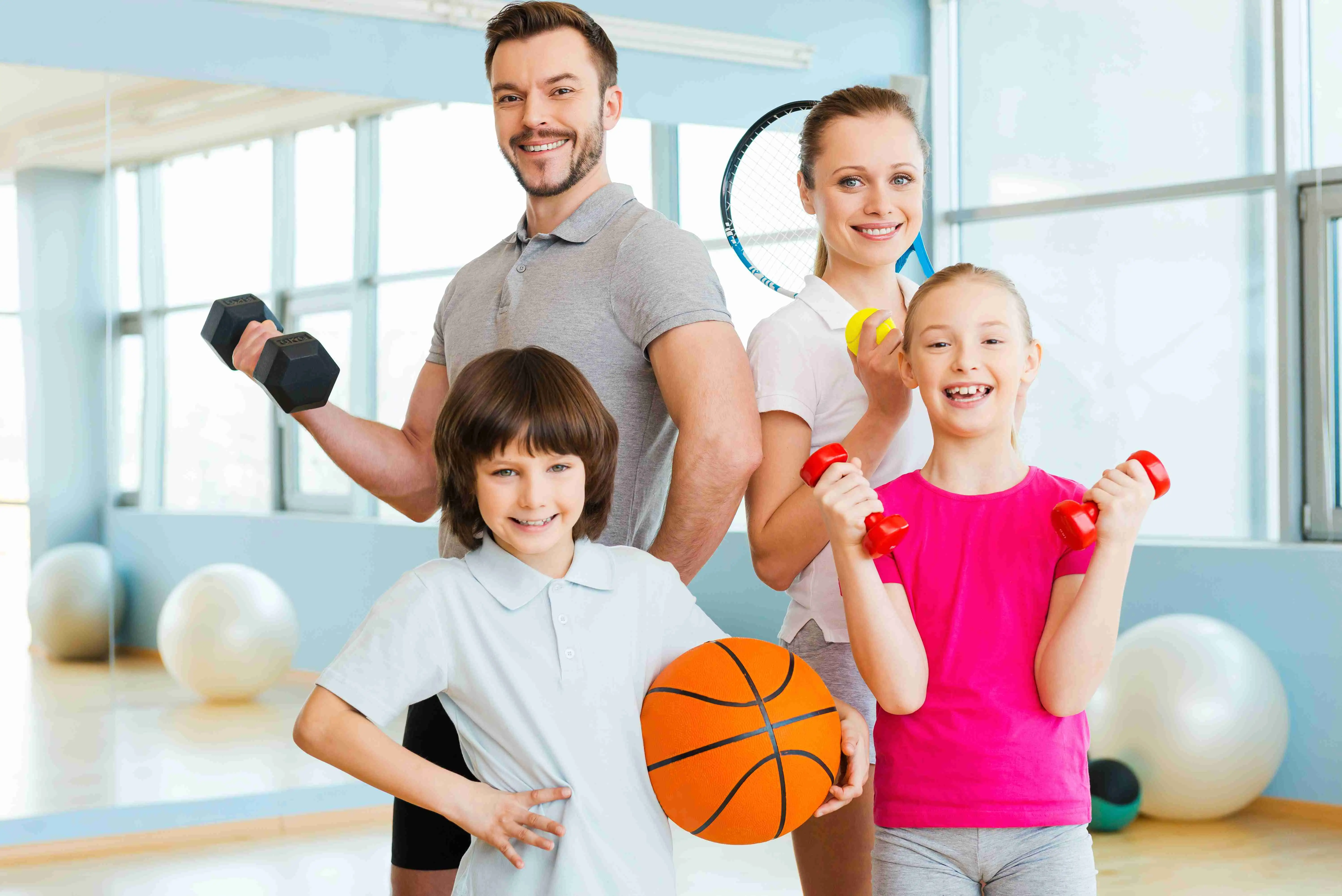 Happy family holding different sports equipment while standing close to each other in health club