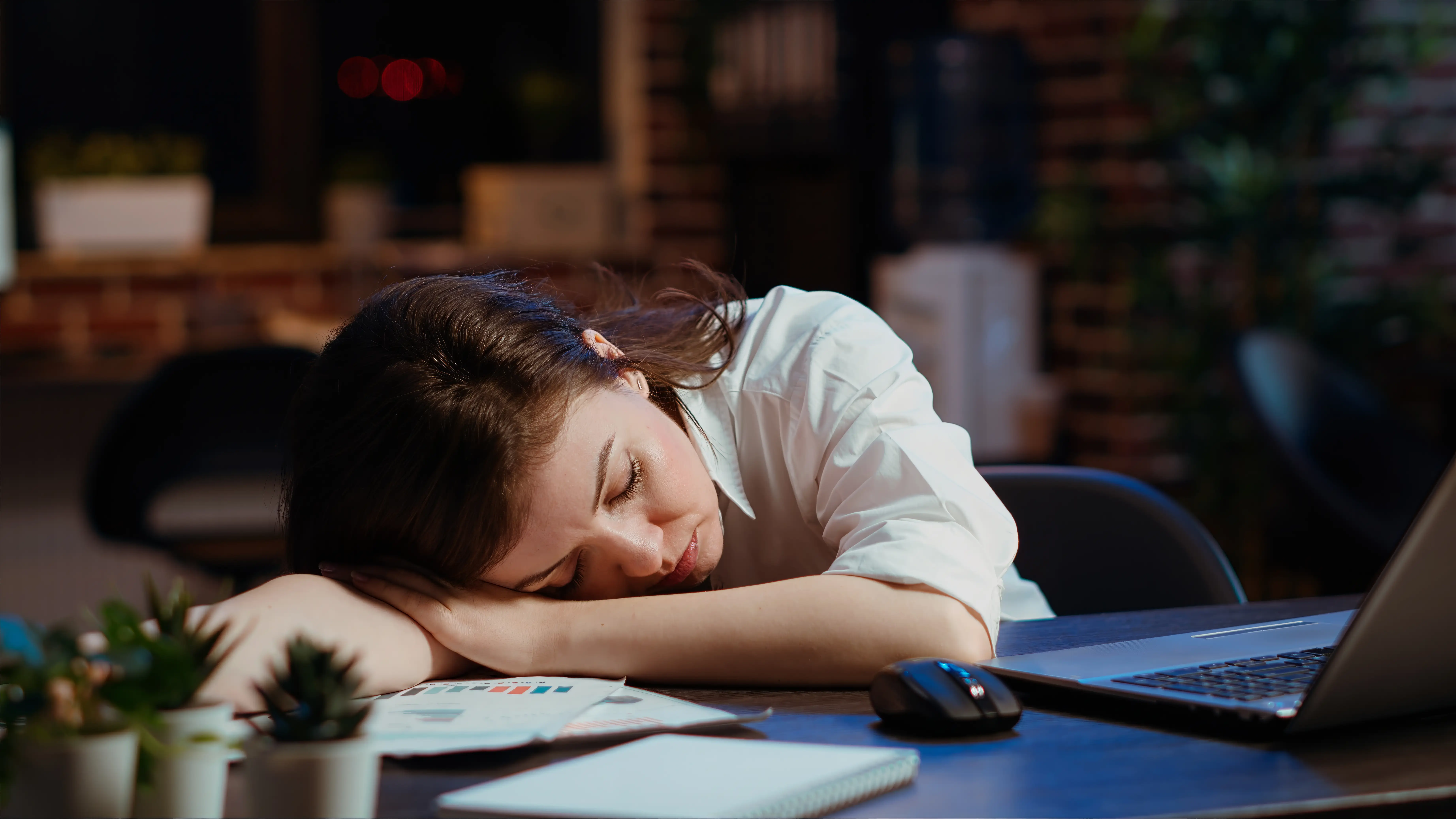 Sleepy employee asleep on computer desk late at night in brick wall office