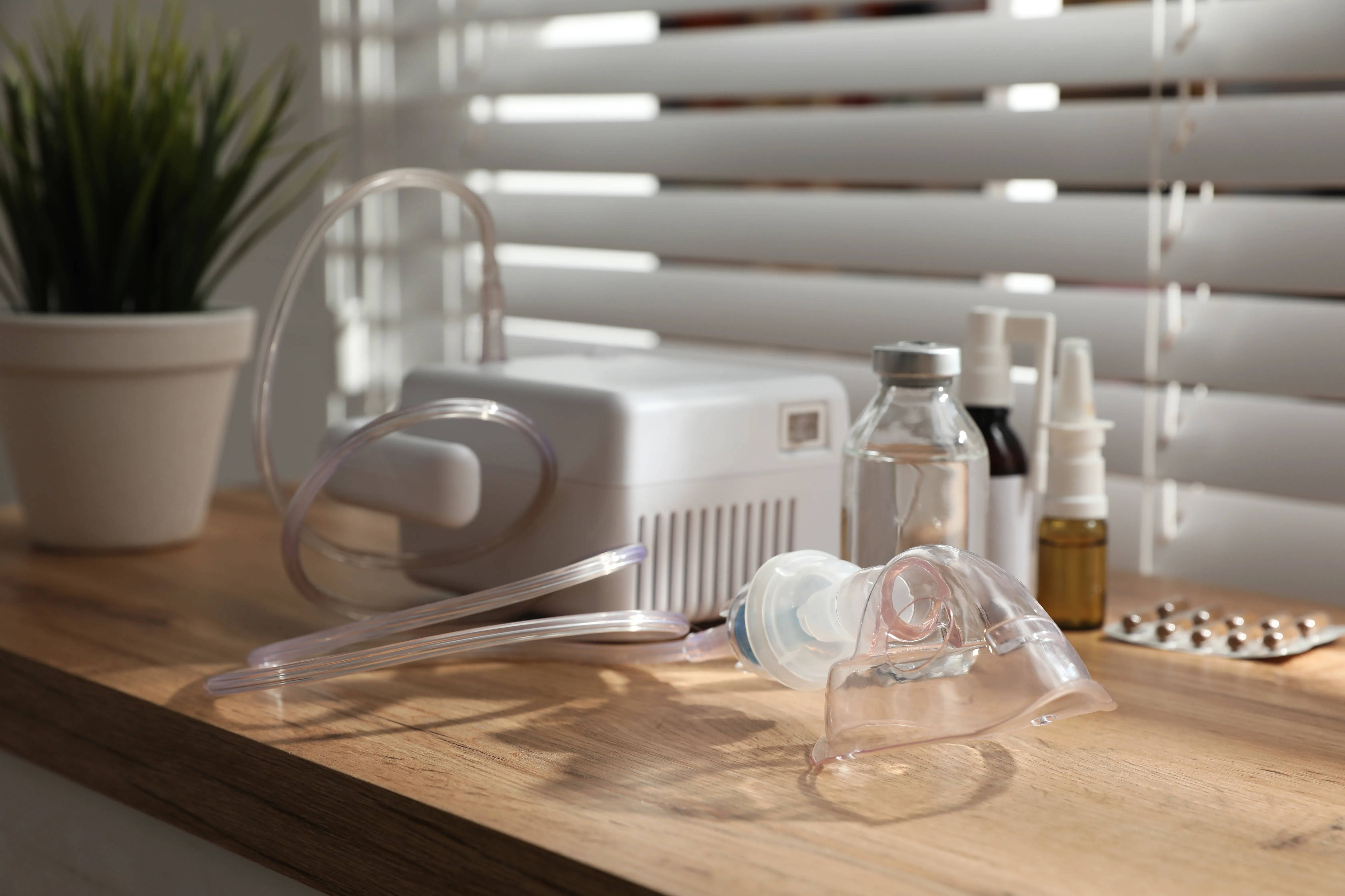 Modern nebulizer with face mask and medications on wooden table indoors. Inhalation equipment