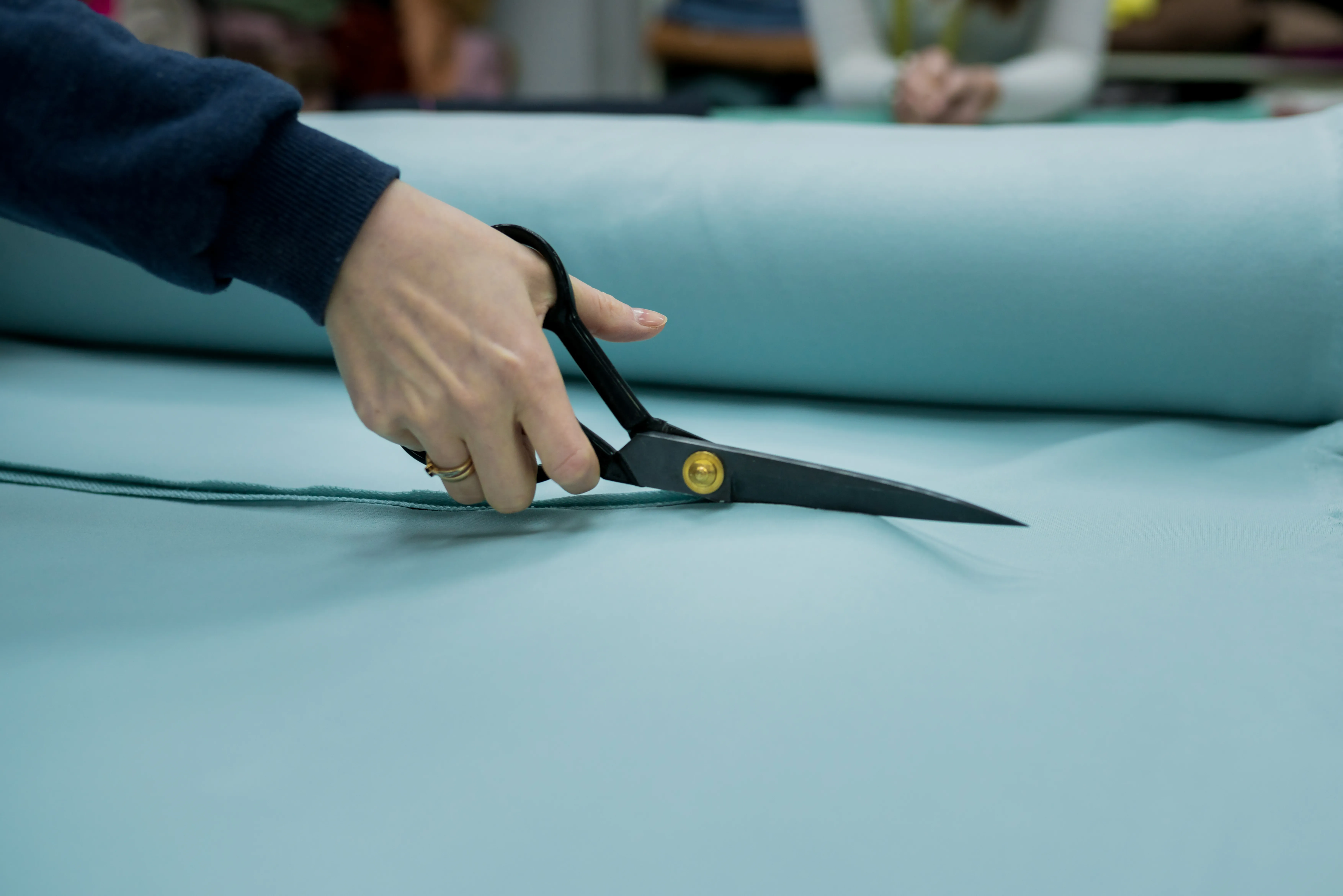 Closeup of seller cutting fabrics in textile store. Seamstress using scissors to trim the material