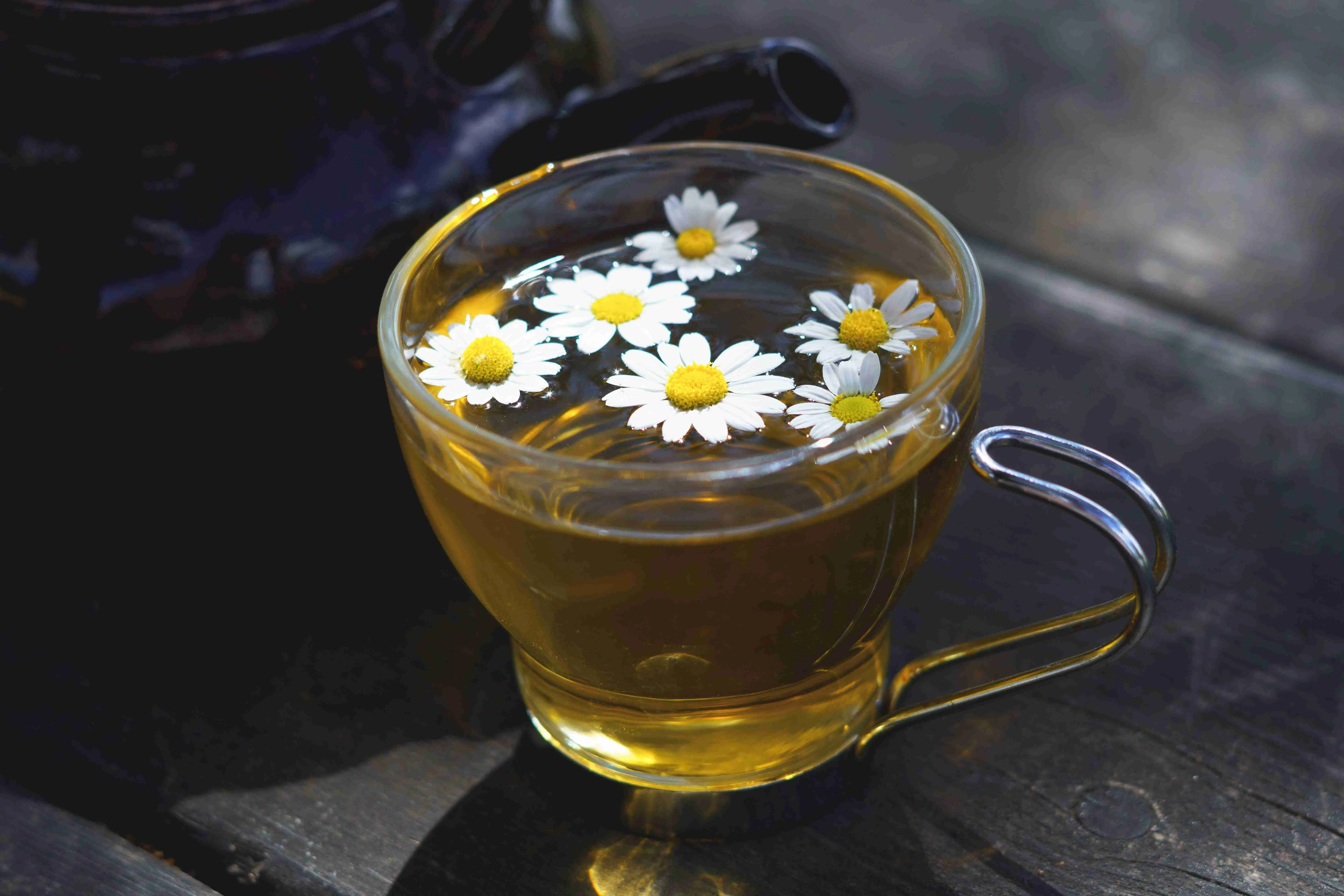 glass cup with a natural chamomile tea and a ceramic teapot