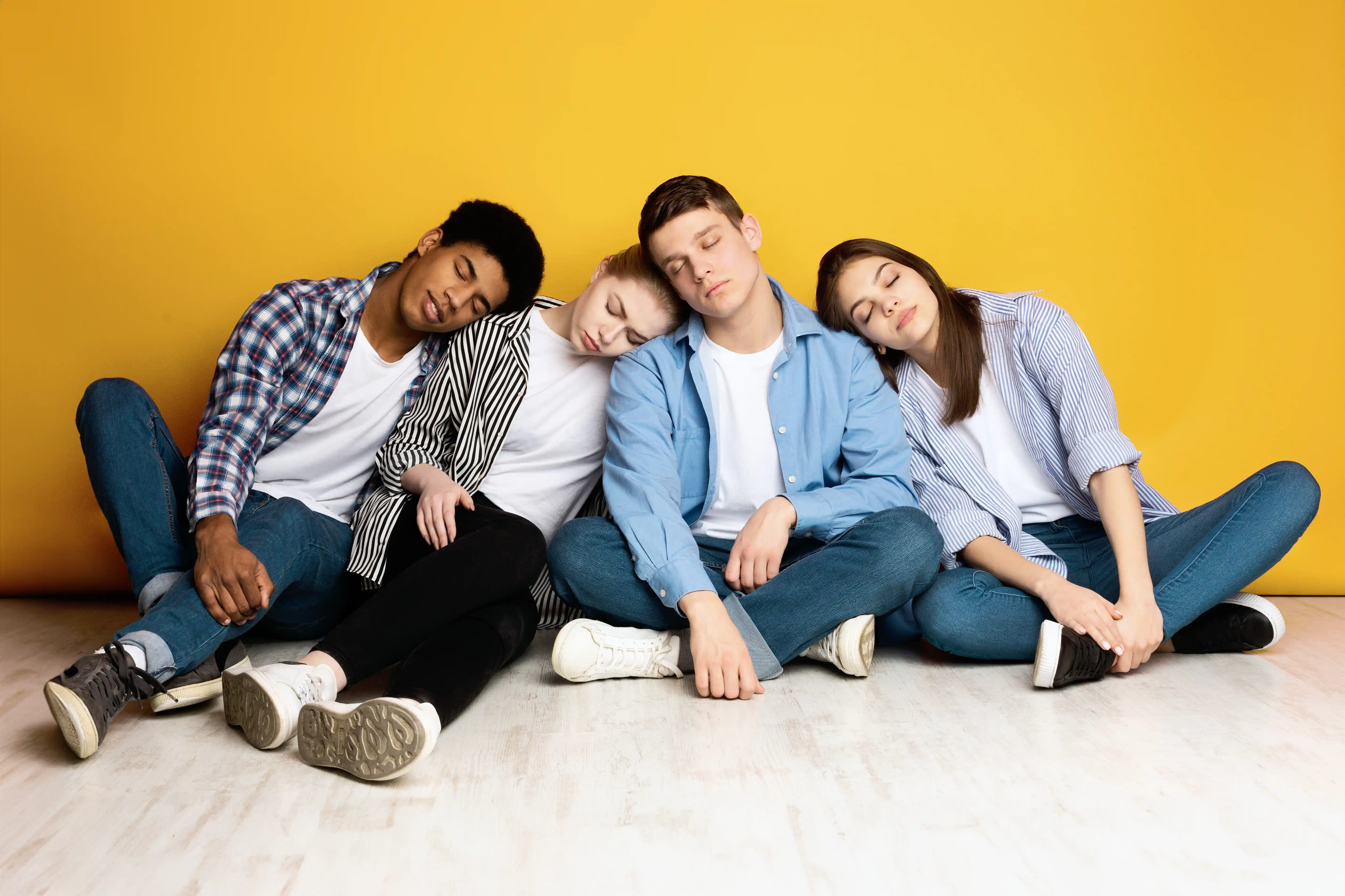 Young Friends Sitting Together and Resting Against a Yellow Wall