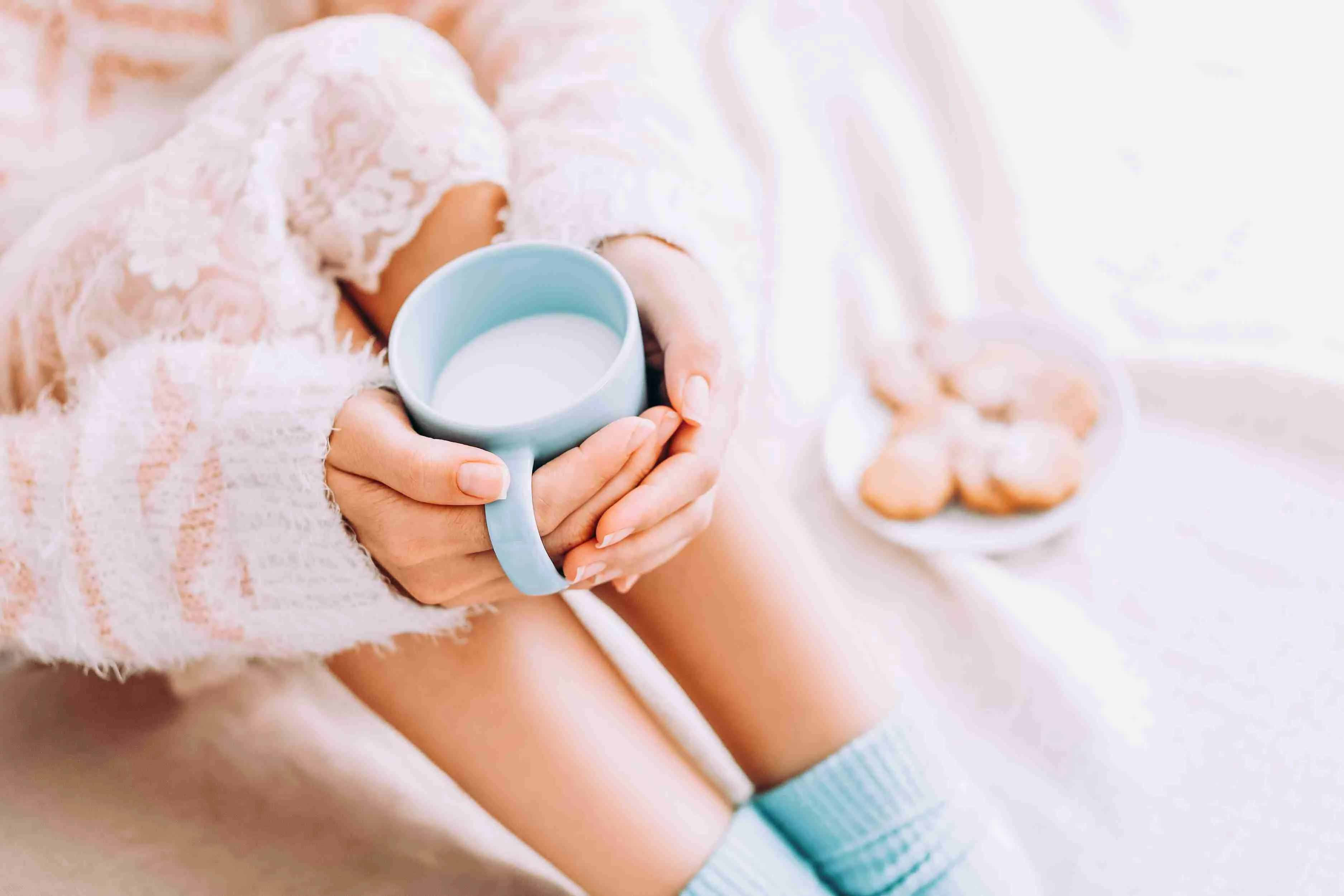 Young woman on the bed with with cup of milk in hands enjoys her stay at home.