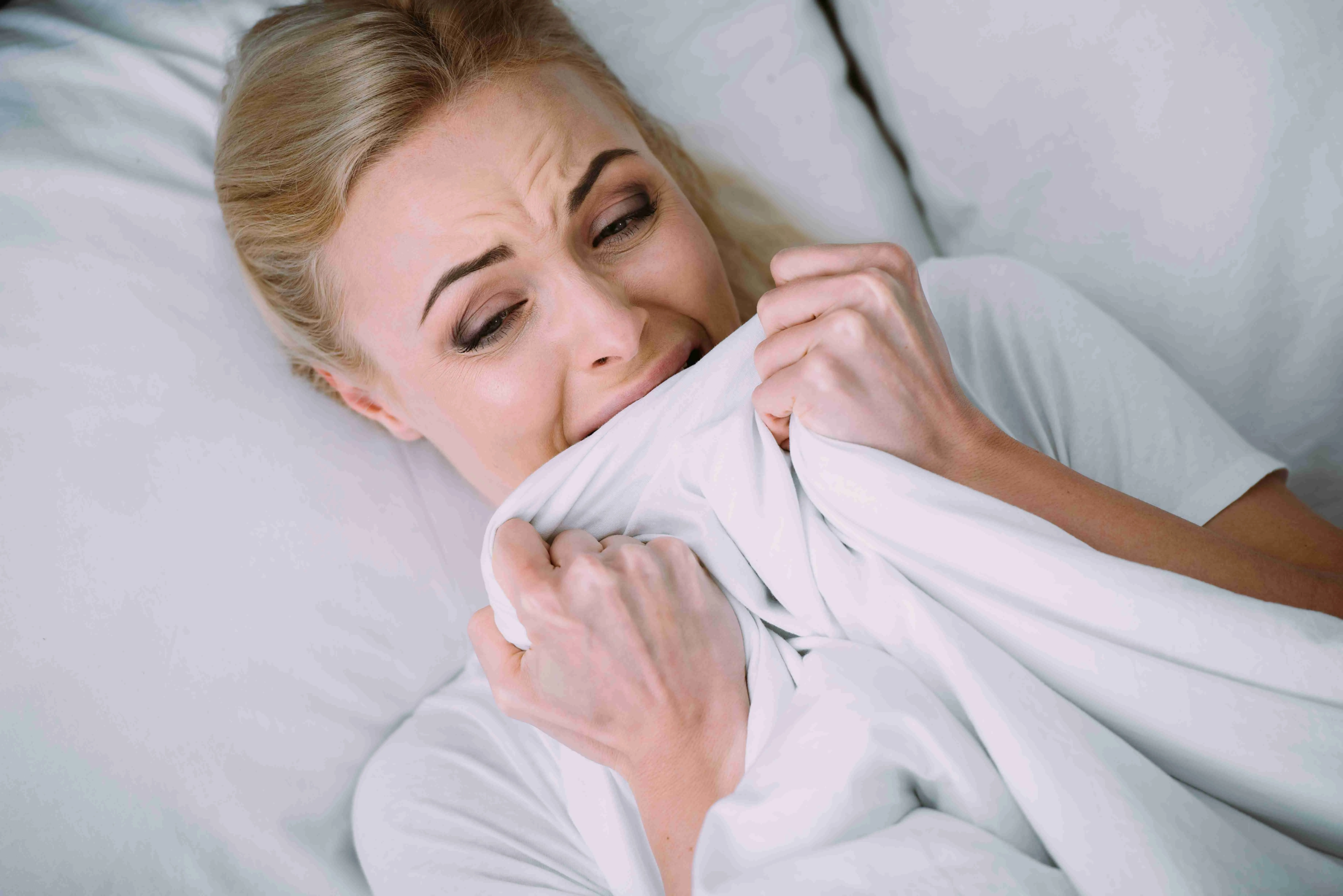 frightened woman lying in bed, crying and holding blanket