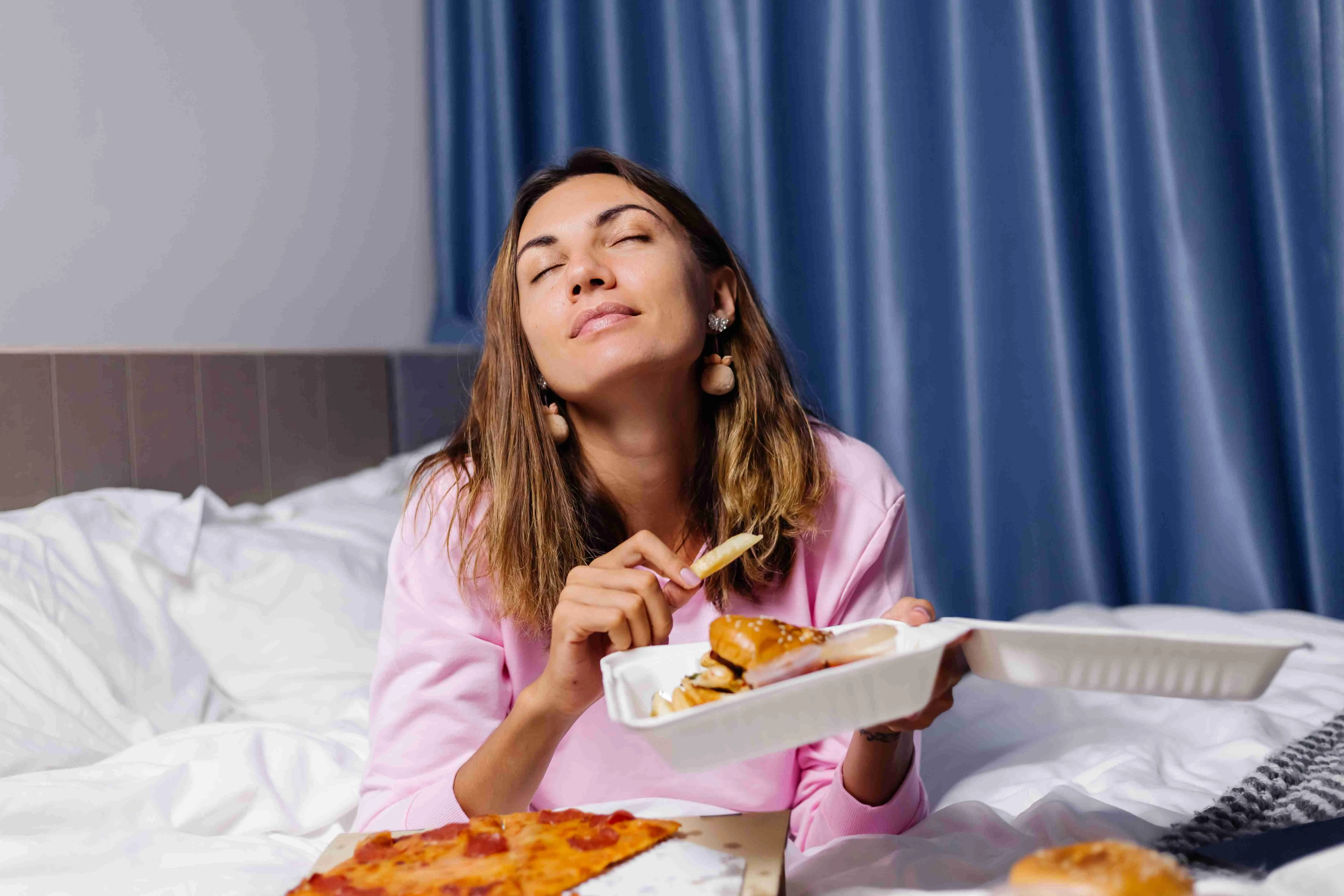 Woman east fast food from delivery on bed in bedroom