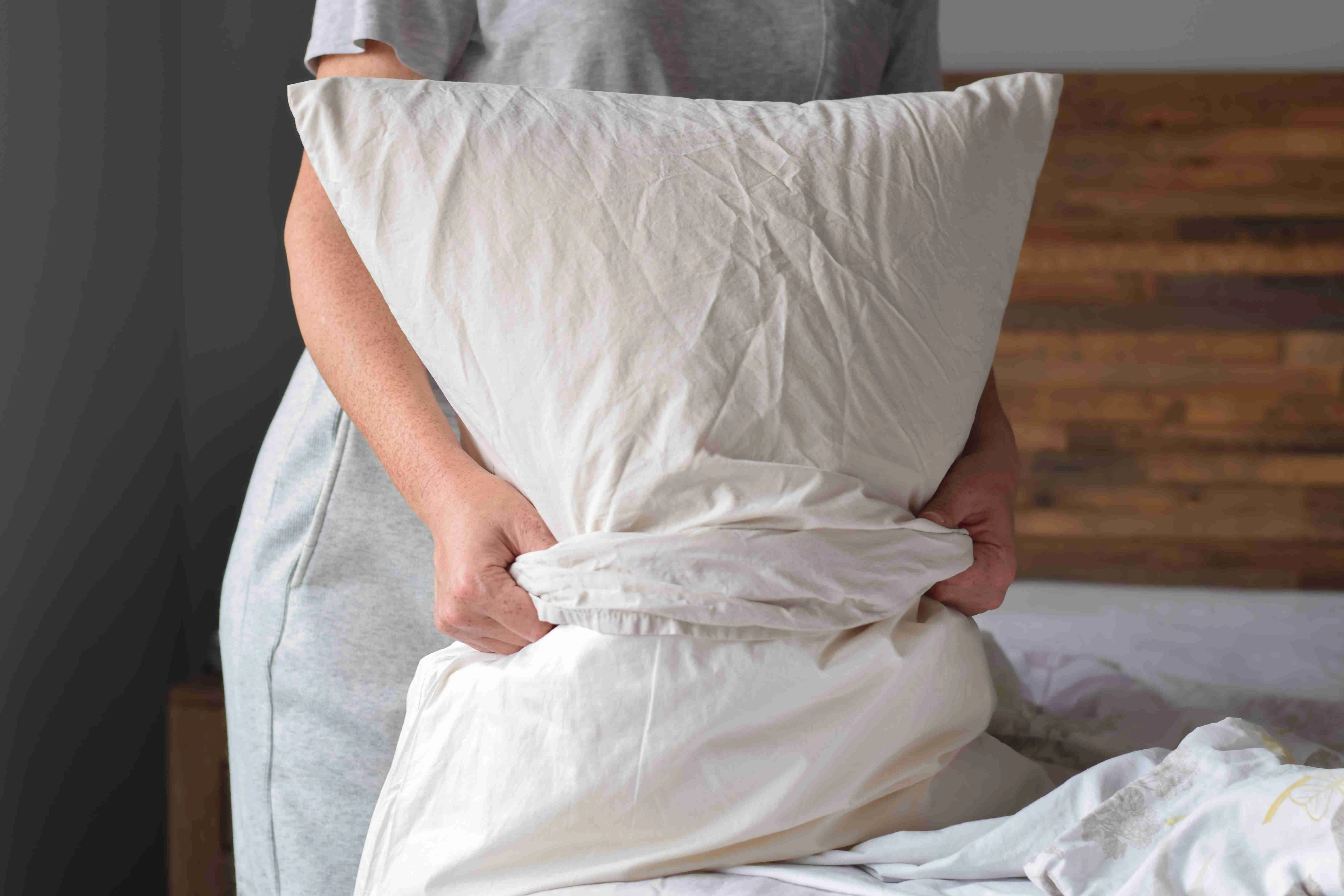 Woman is putting pillowcase on a pillow while changing bed sheets