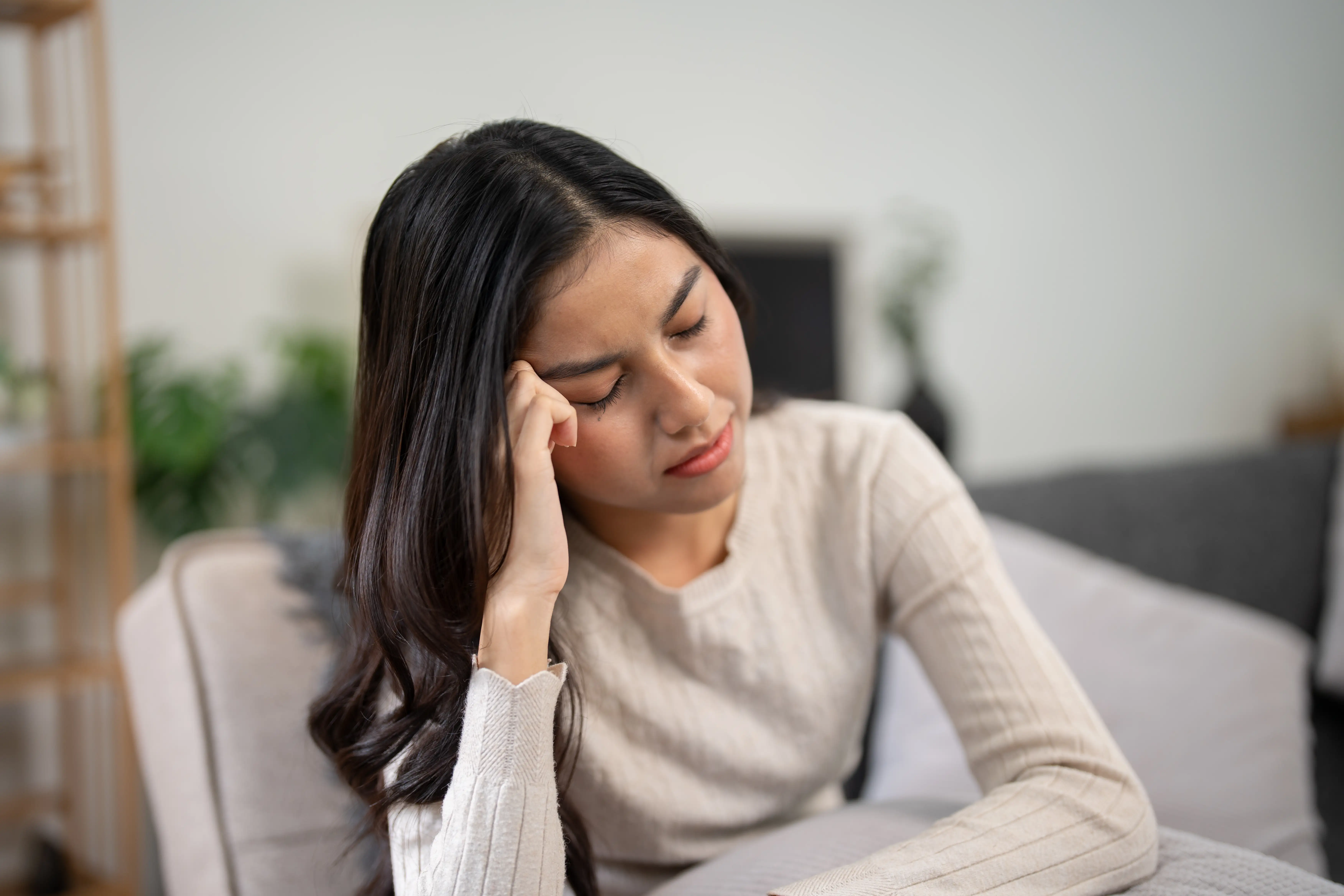 Young woman with head pain sitting on a couch at home