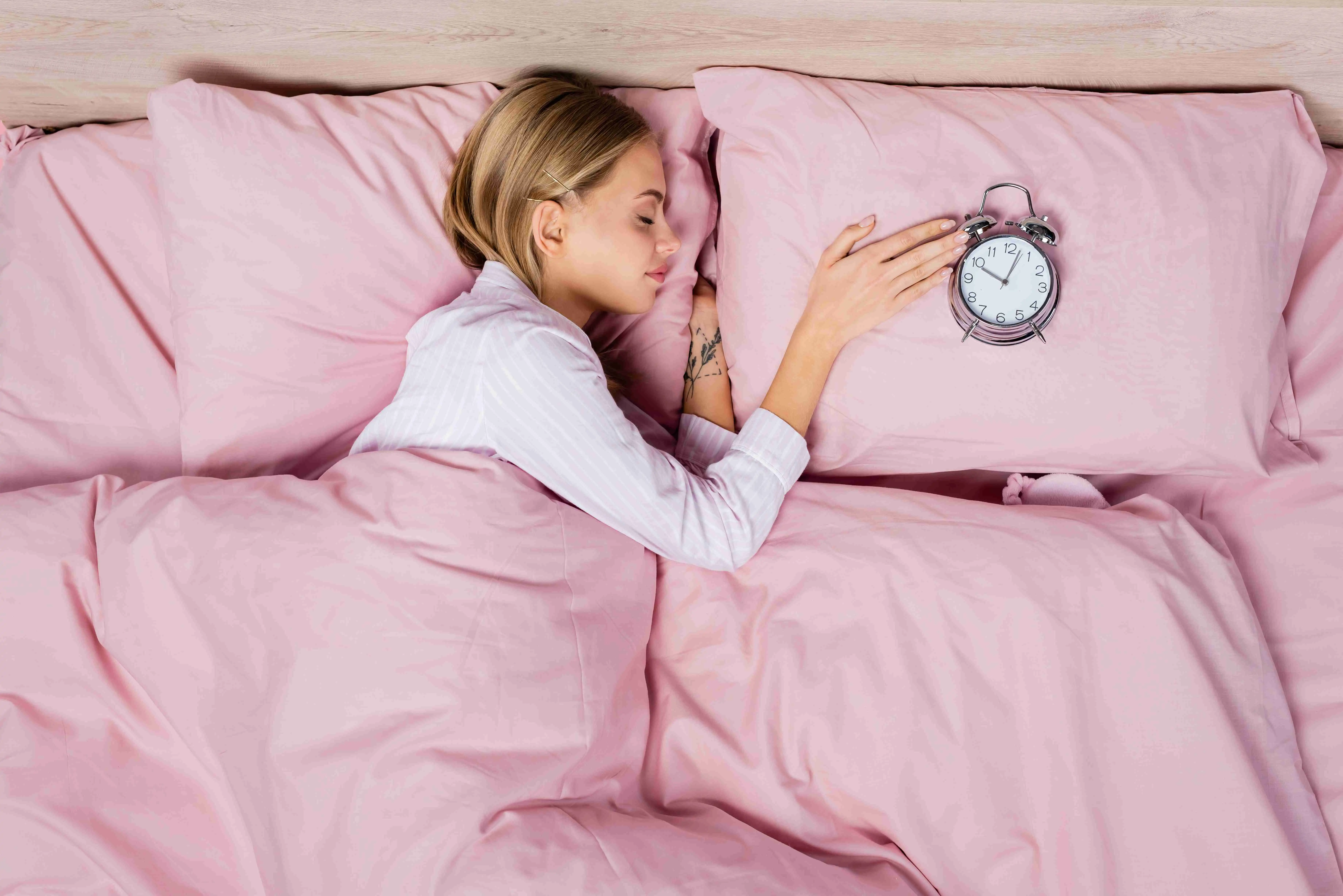 Top view of young woman sleeping near alarm clock on pillow on bed