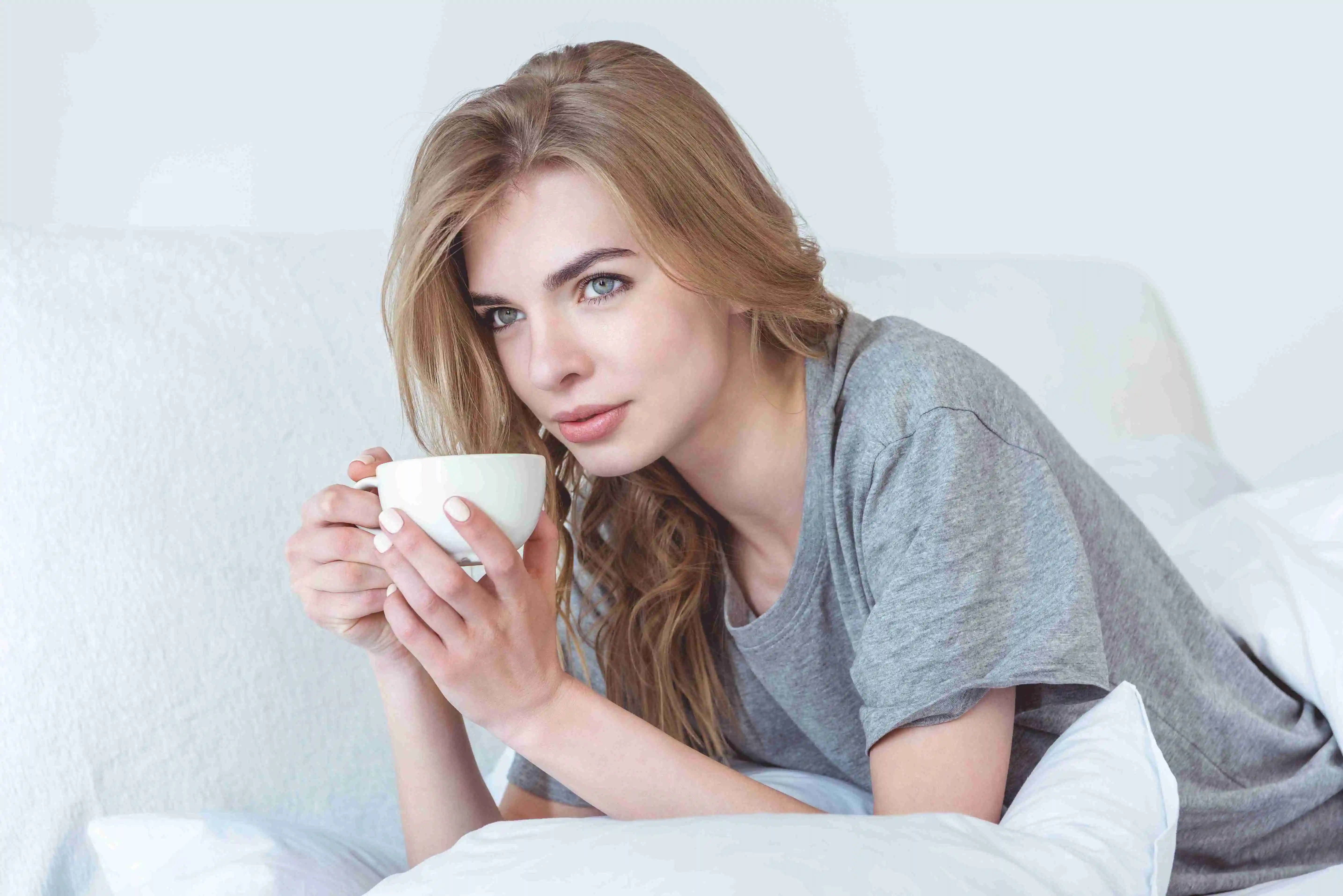 attractive blonde woman drinking coffee and relaxing in bed