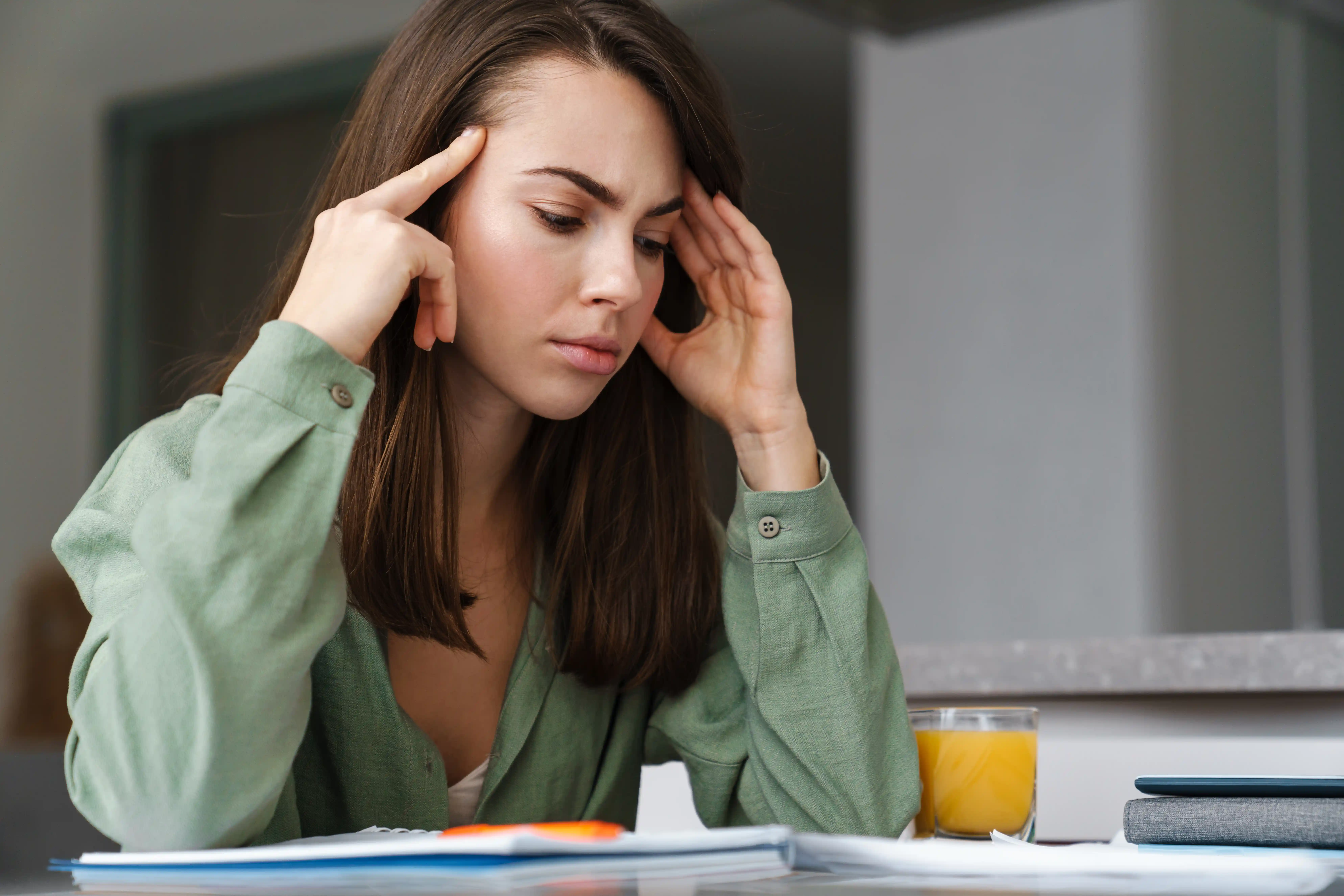Young white woman with headache working with paper at home kitchen