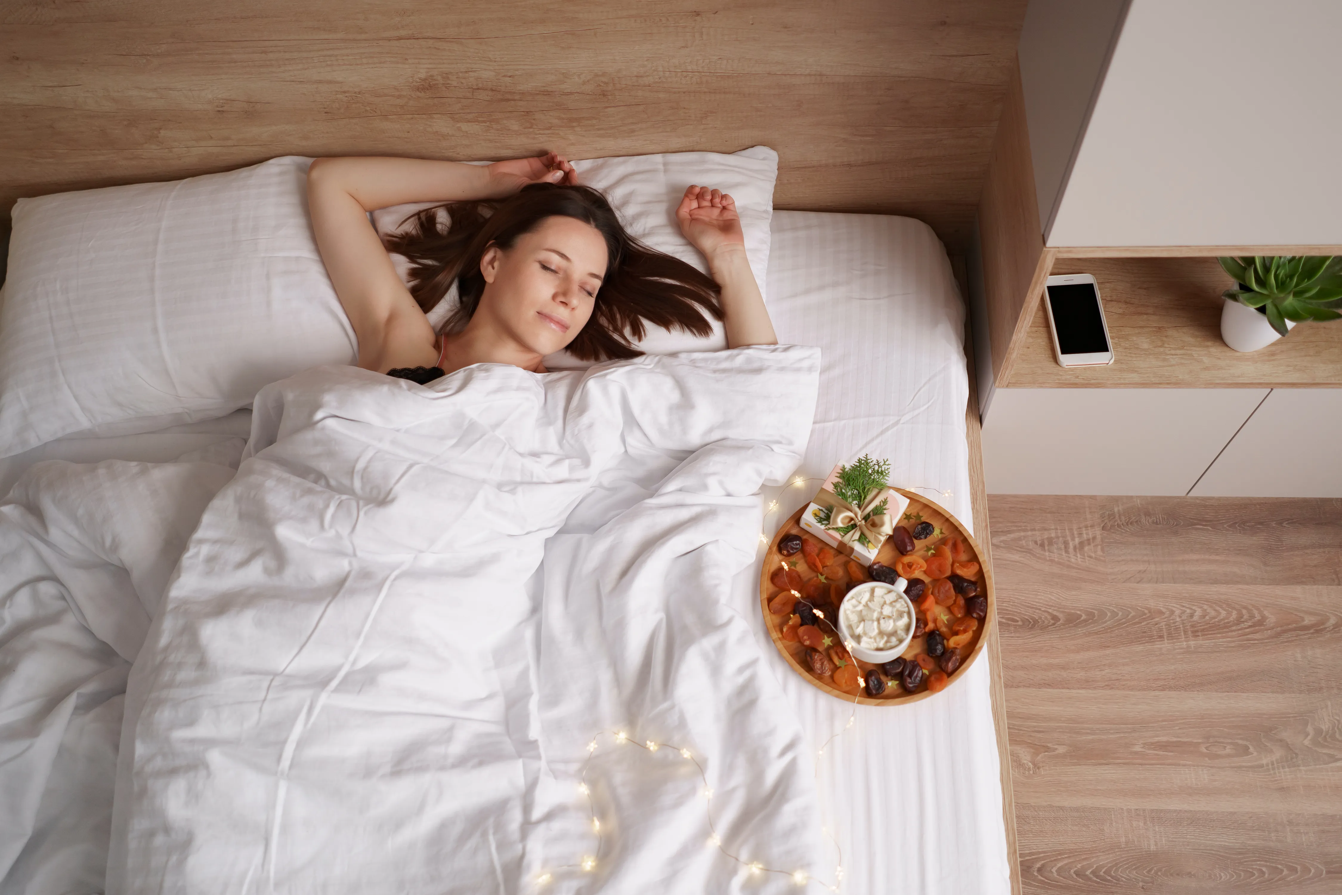 Woman sleeping on the bed with present and coffee with marshmallows standing near her. Morning surprise