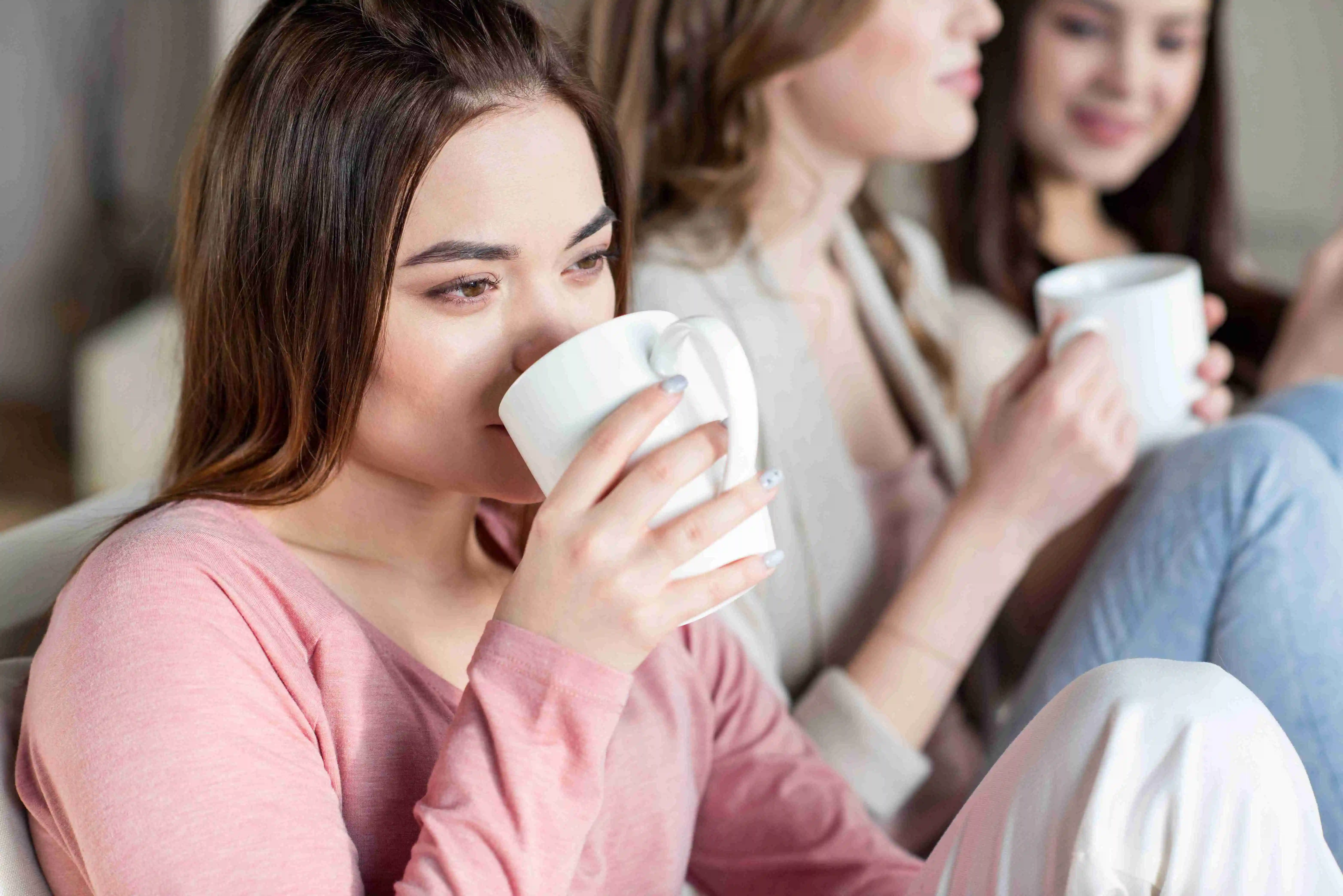 Attractive young women drinking hot beverages from white cups