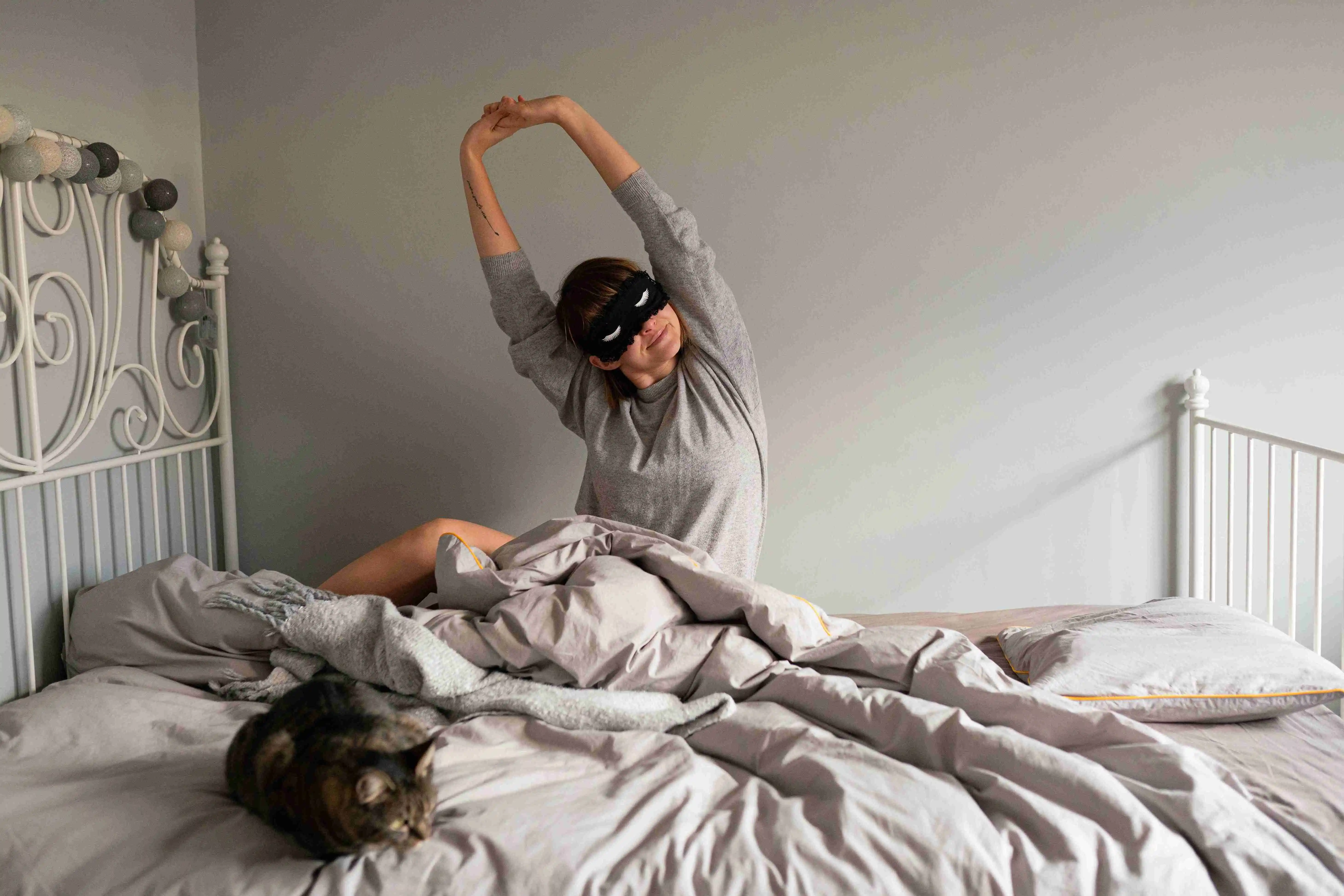 young woman with sleep mask stretching in bed