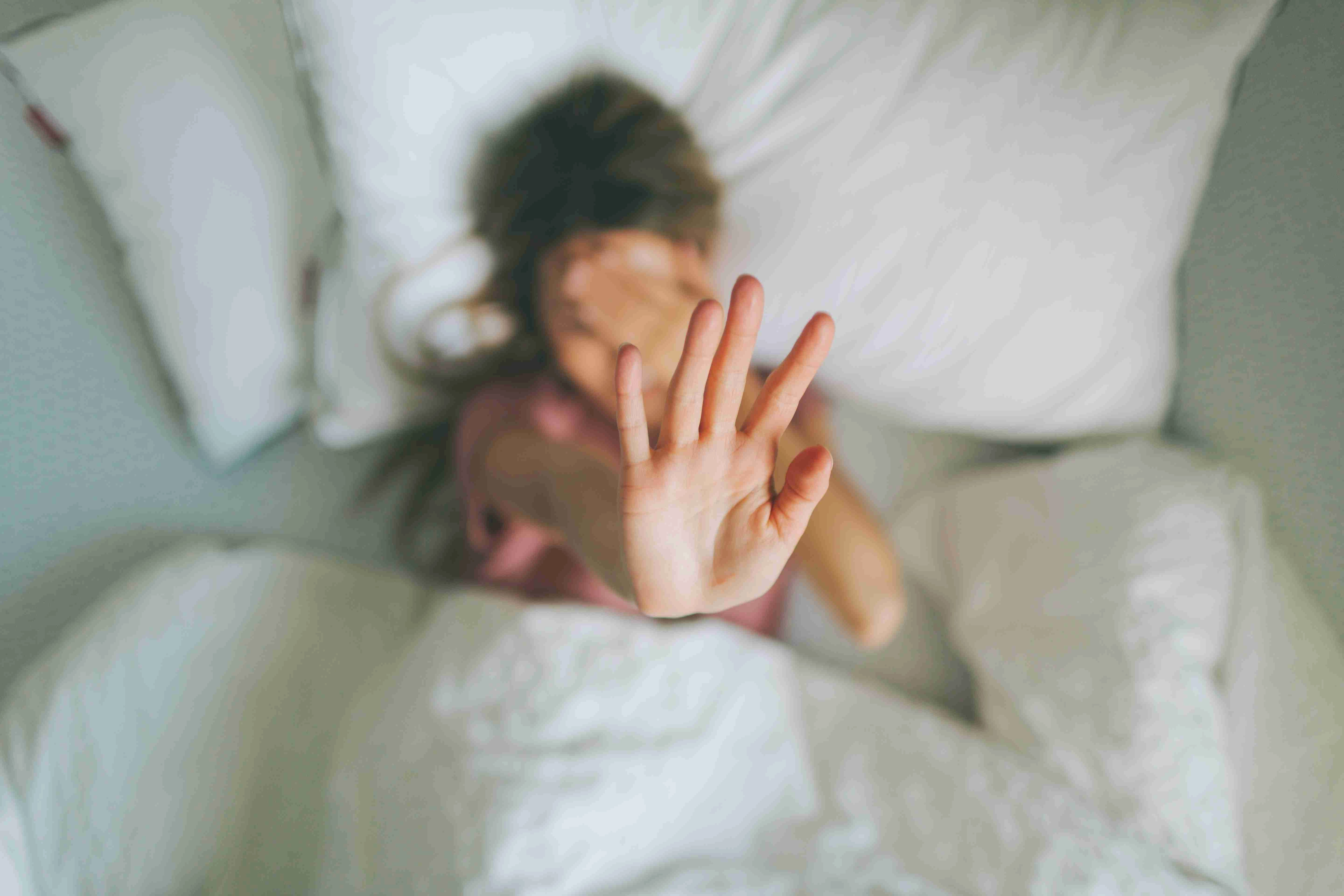 A woman covering her face with her hands, who wants to stay in bed.