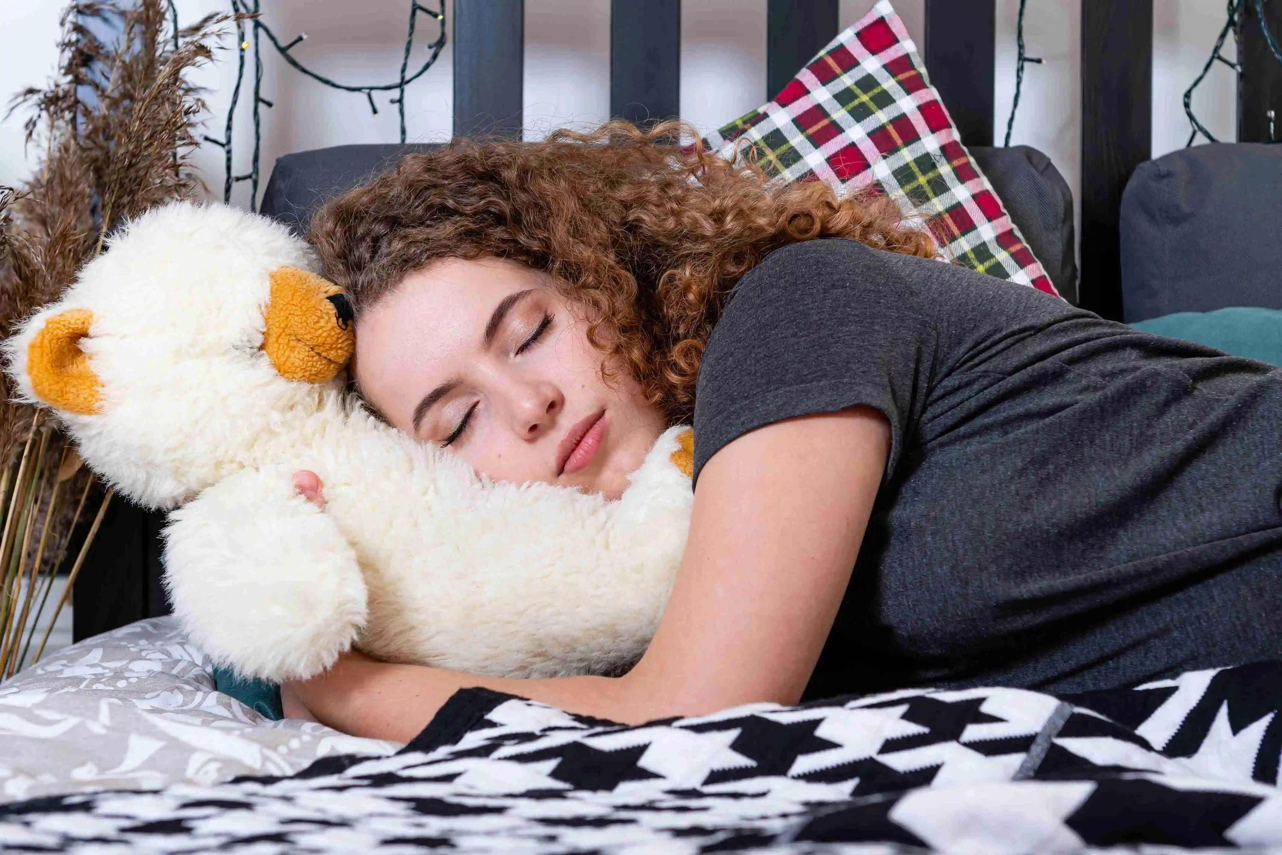 a young curly teenager woman with a teddy bear fell asleep in bed