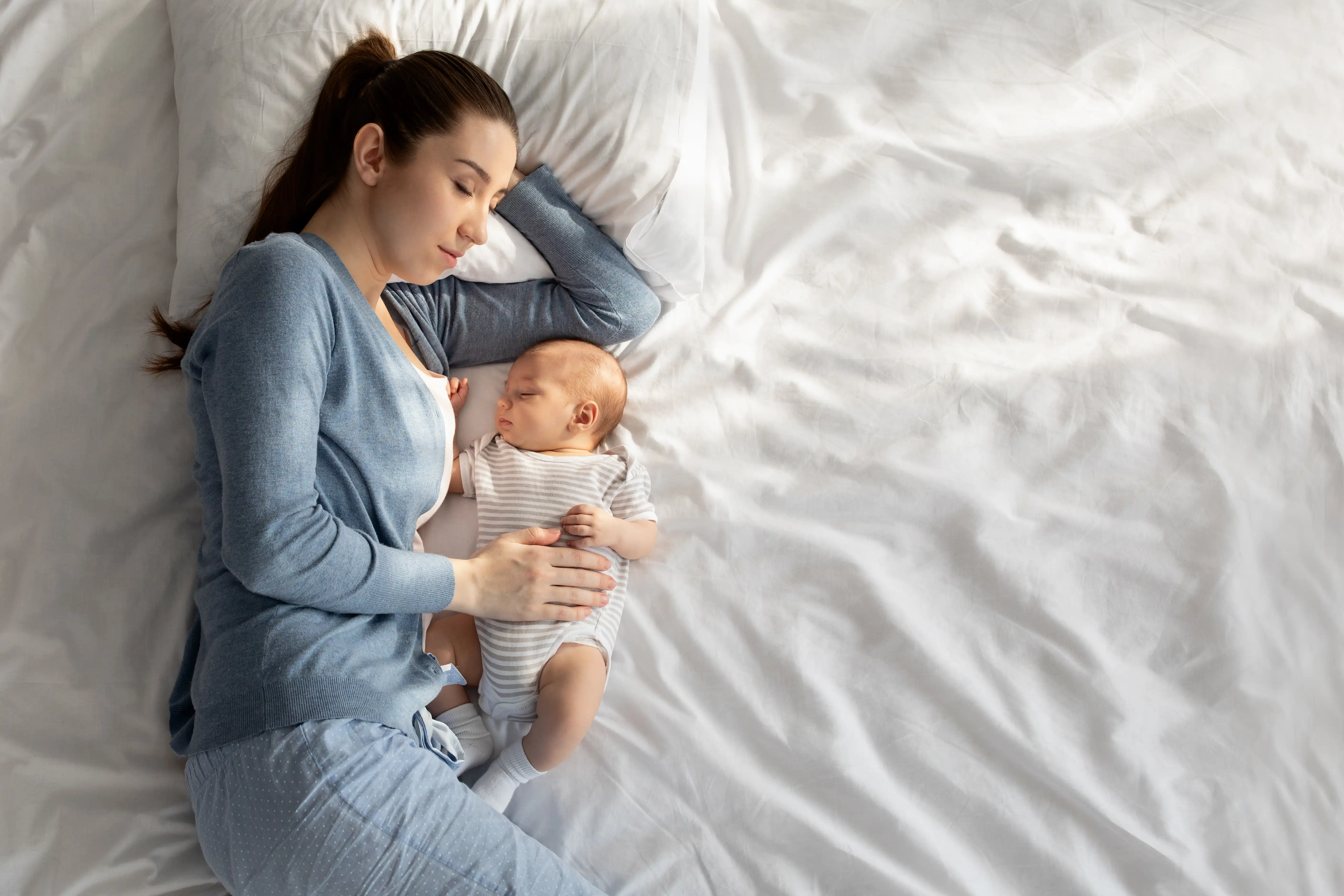 Young woman napping in bed with her cute newborn child