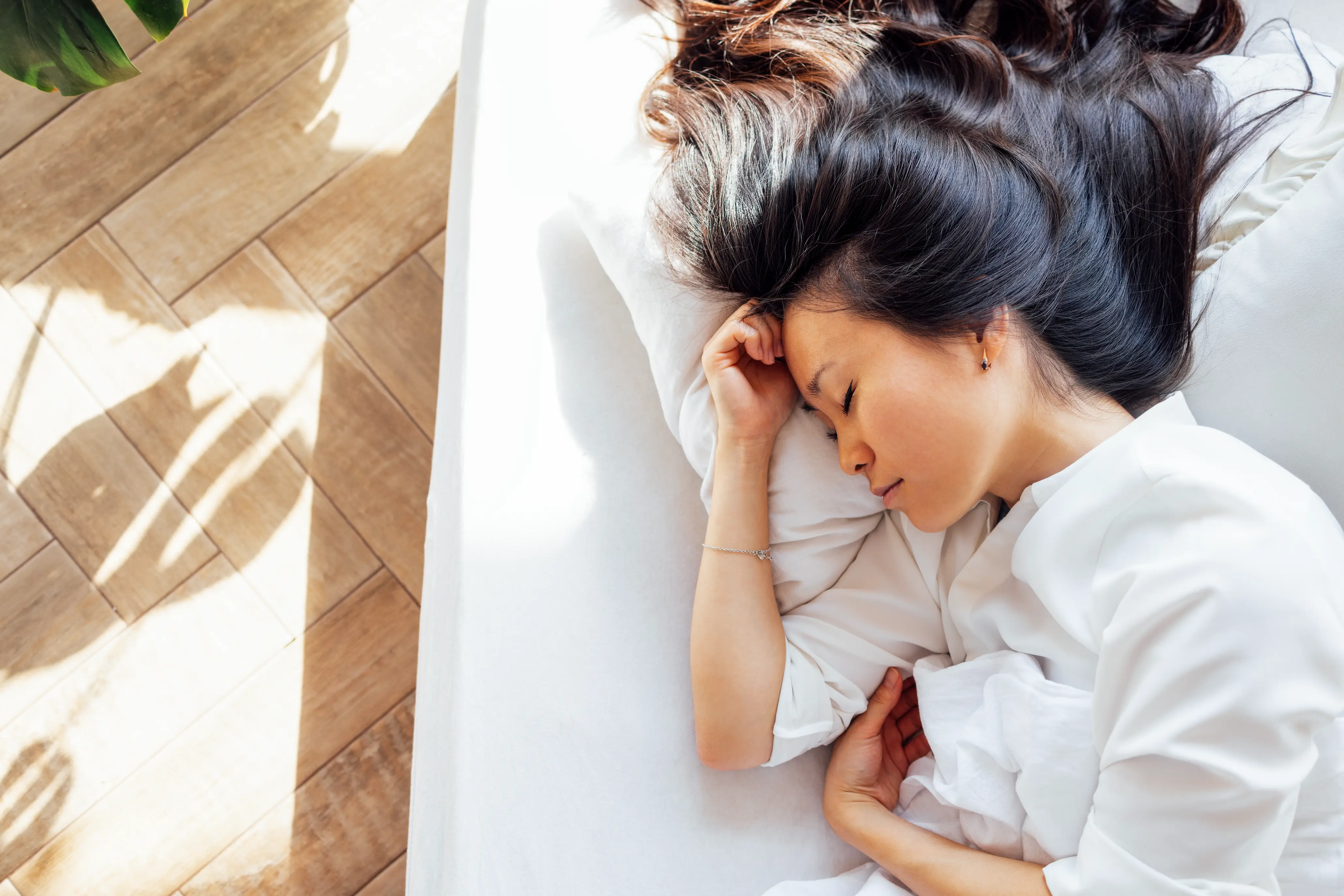 Attractive happy Asian woman lies on a white linen bed in the morning