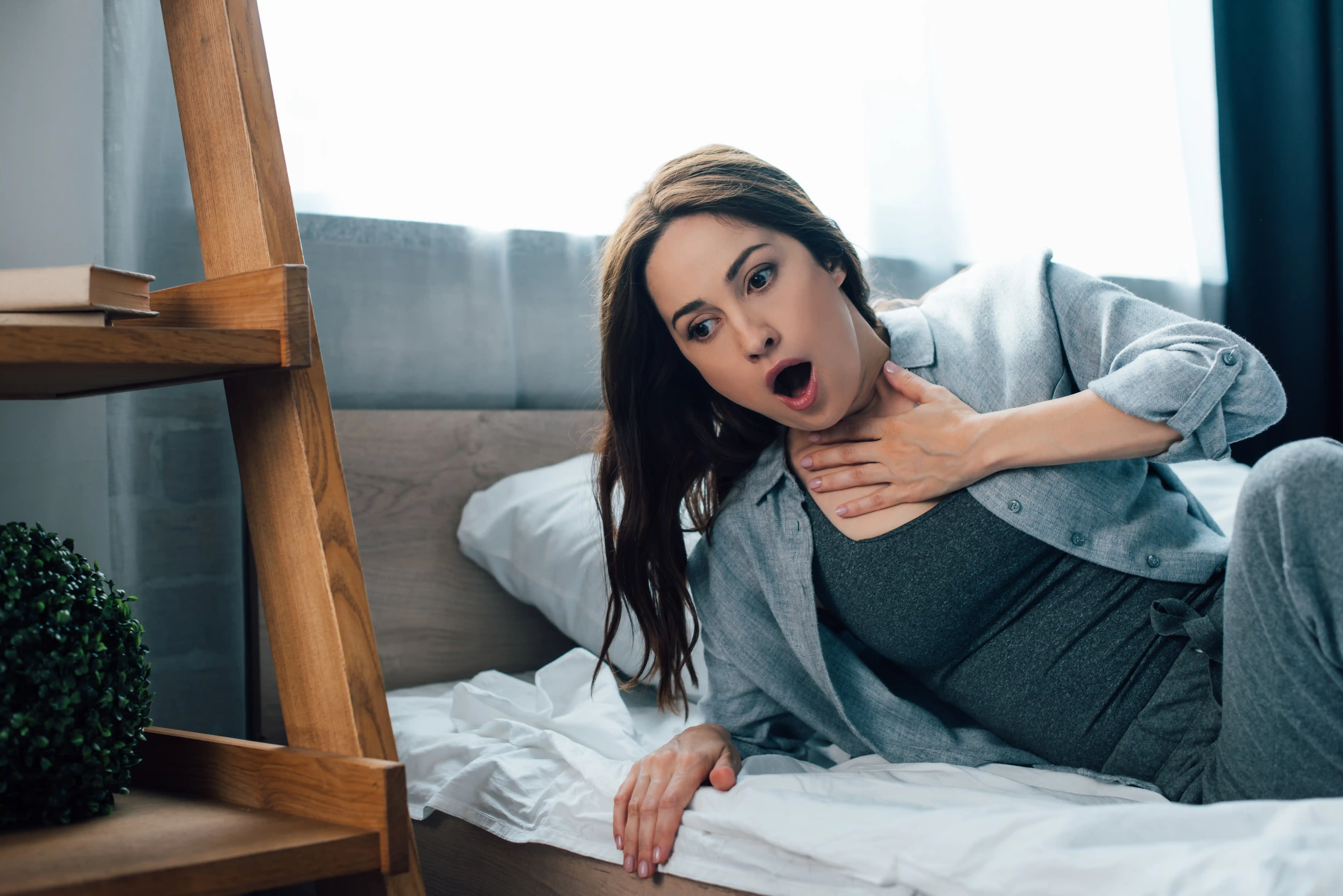 frightened brunette woman touching throat in bedroom
