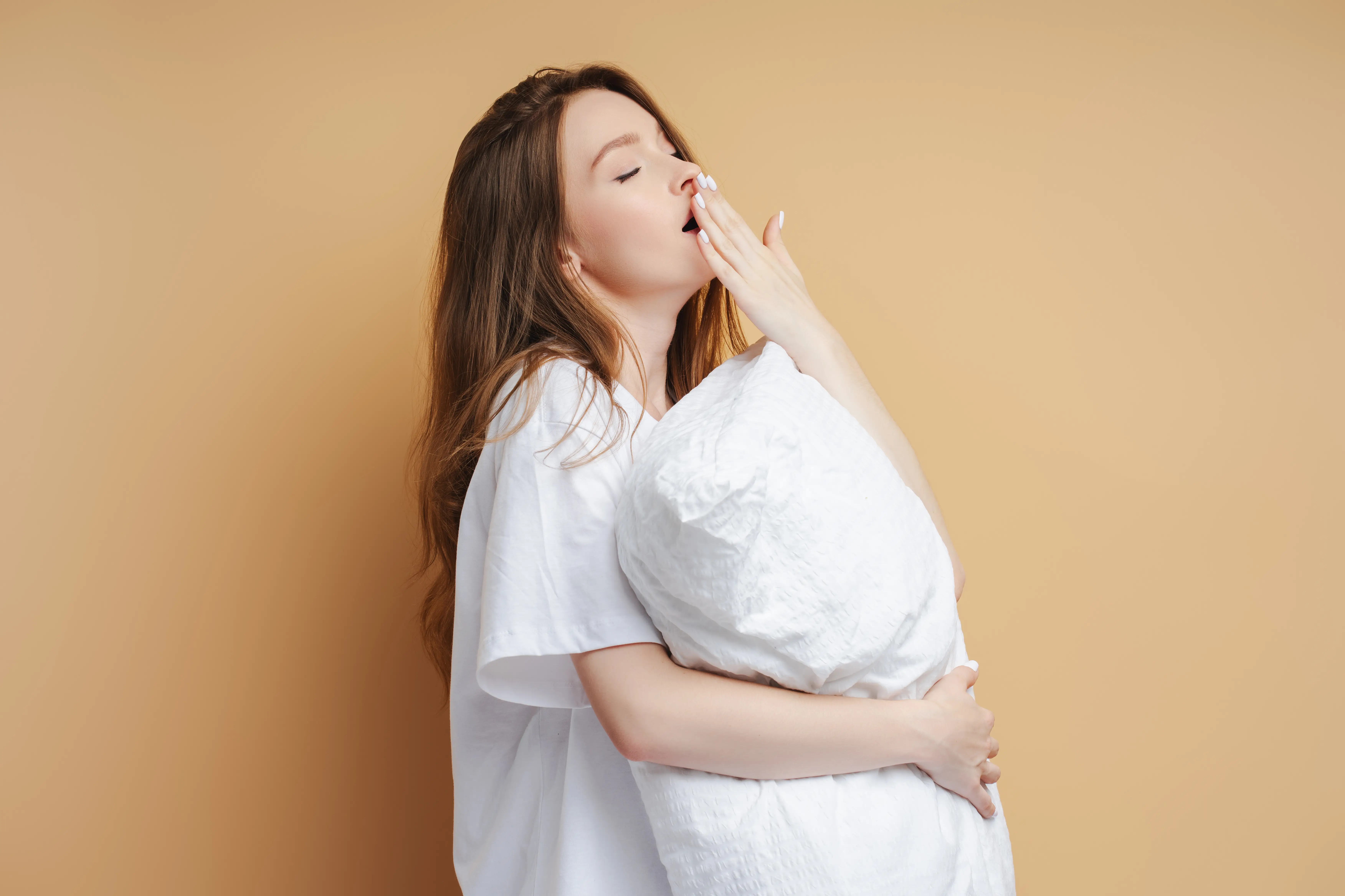 Young cute caucasian woman sleeping, yawning, holding comfortable white pillow