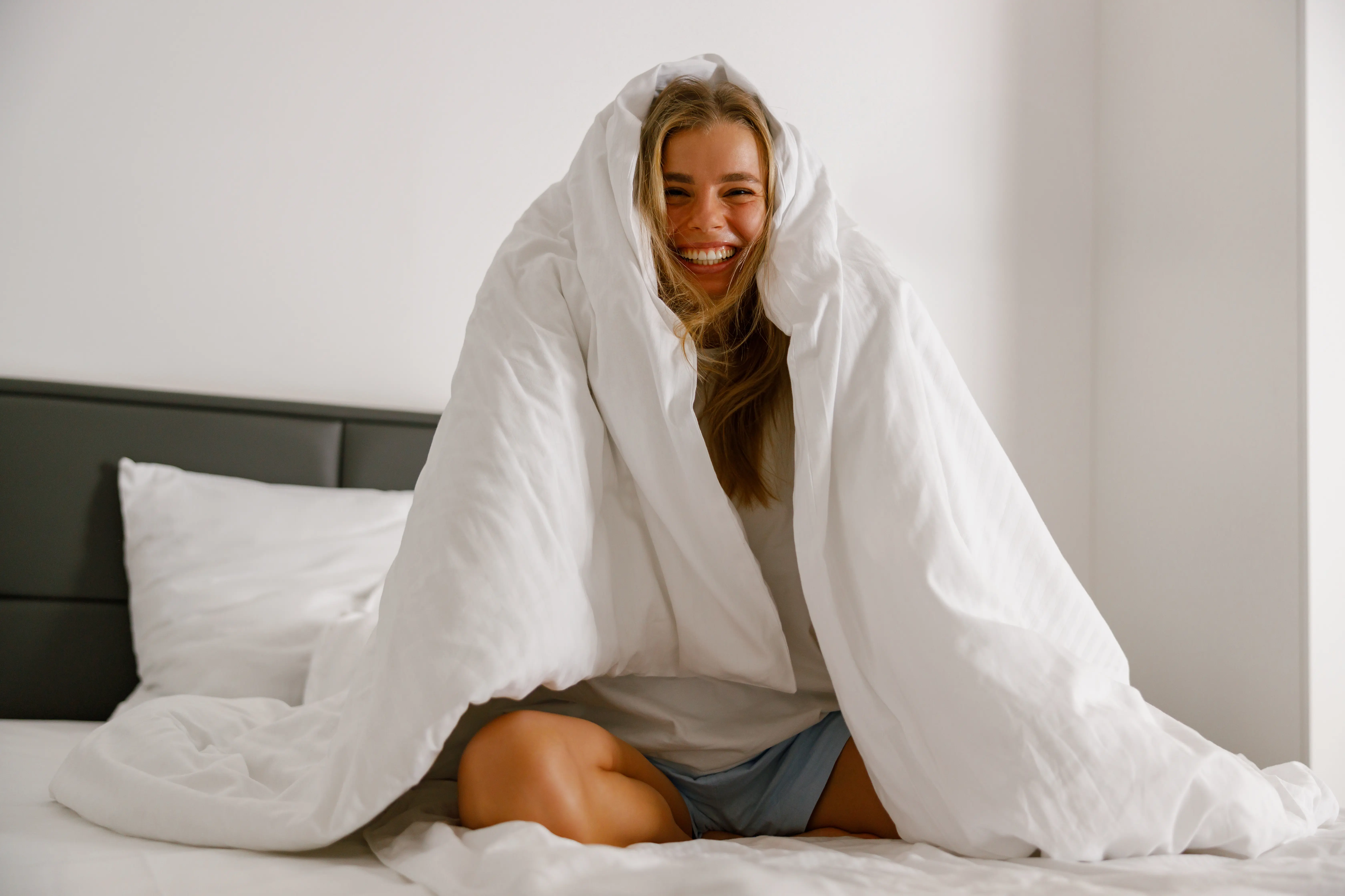 A cheerful young woman snugly wrapped in a warm blanket, radiating happiness and comfort in her cozy bedroom