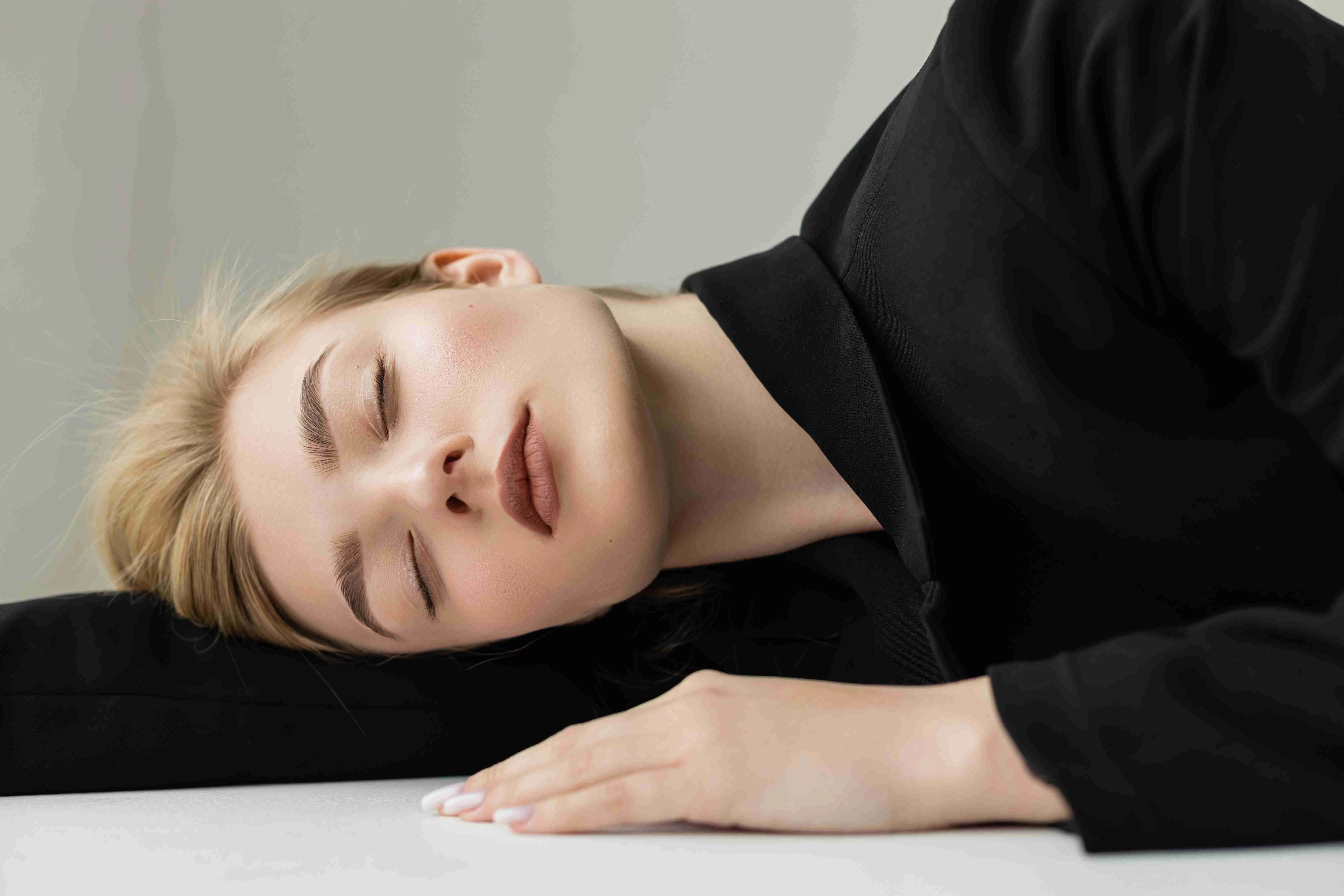 pretty woman in black blazer lying with closed eyes on white surface and grey background