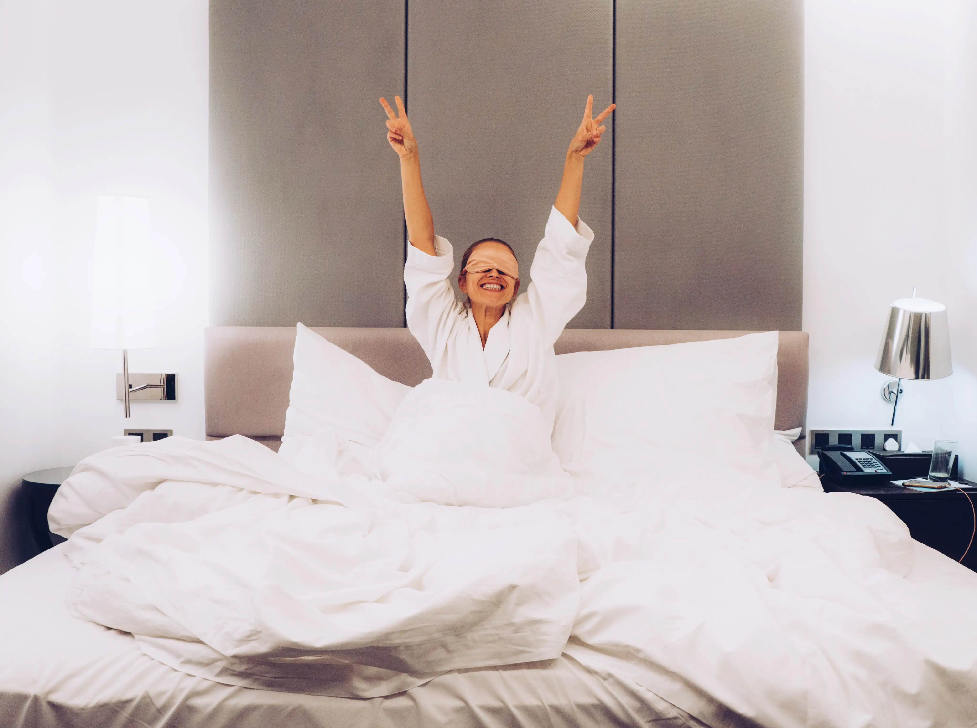 Woman smiling after waking up in bed with her hands raised up