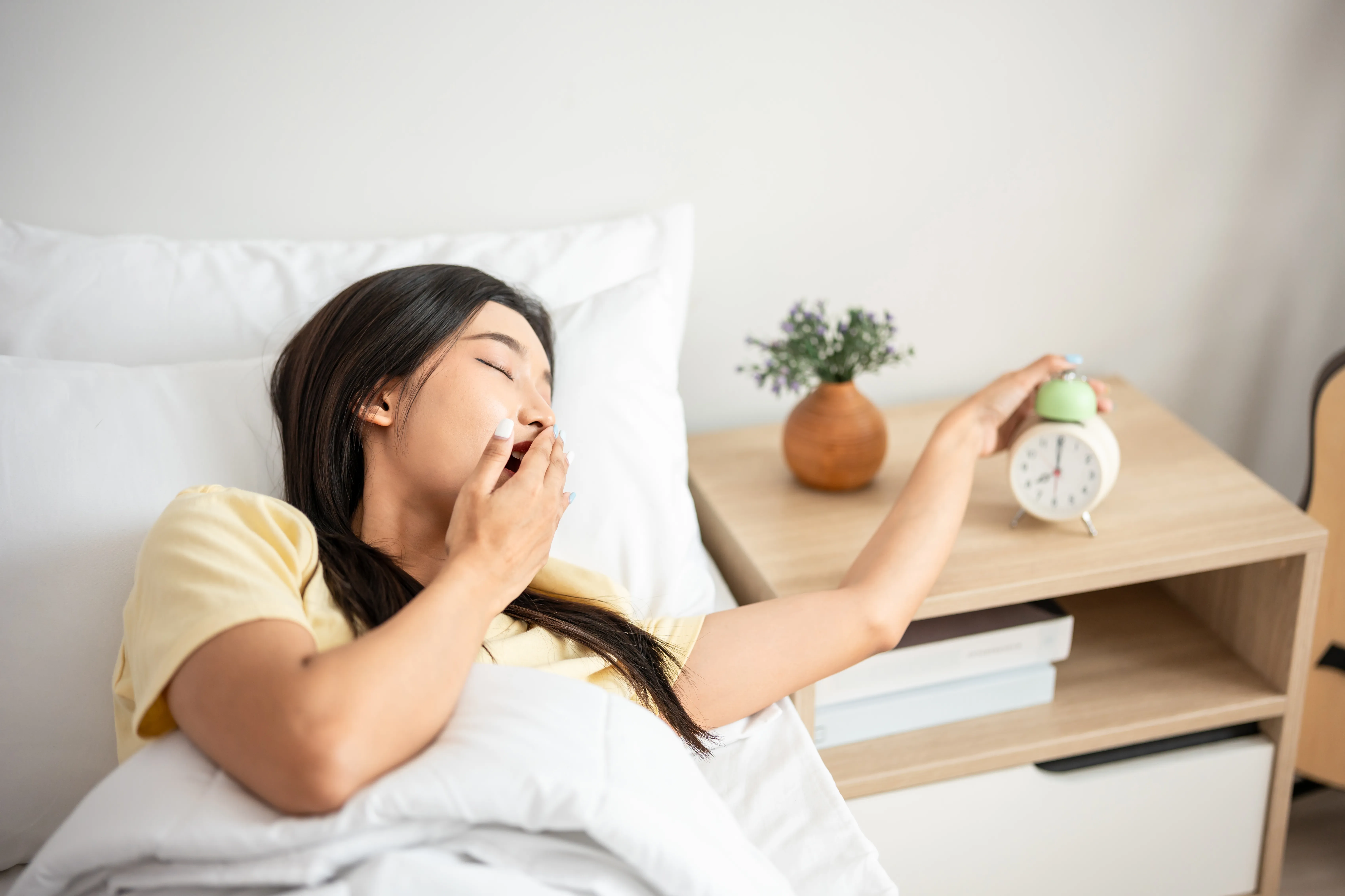 Asian beautiful tired young woman turn off an alarm clock in morning.