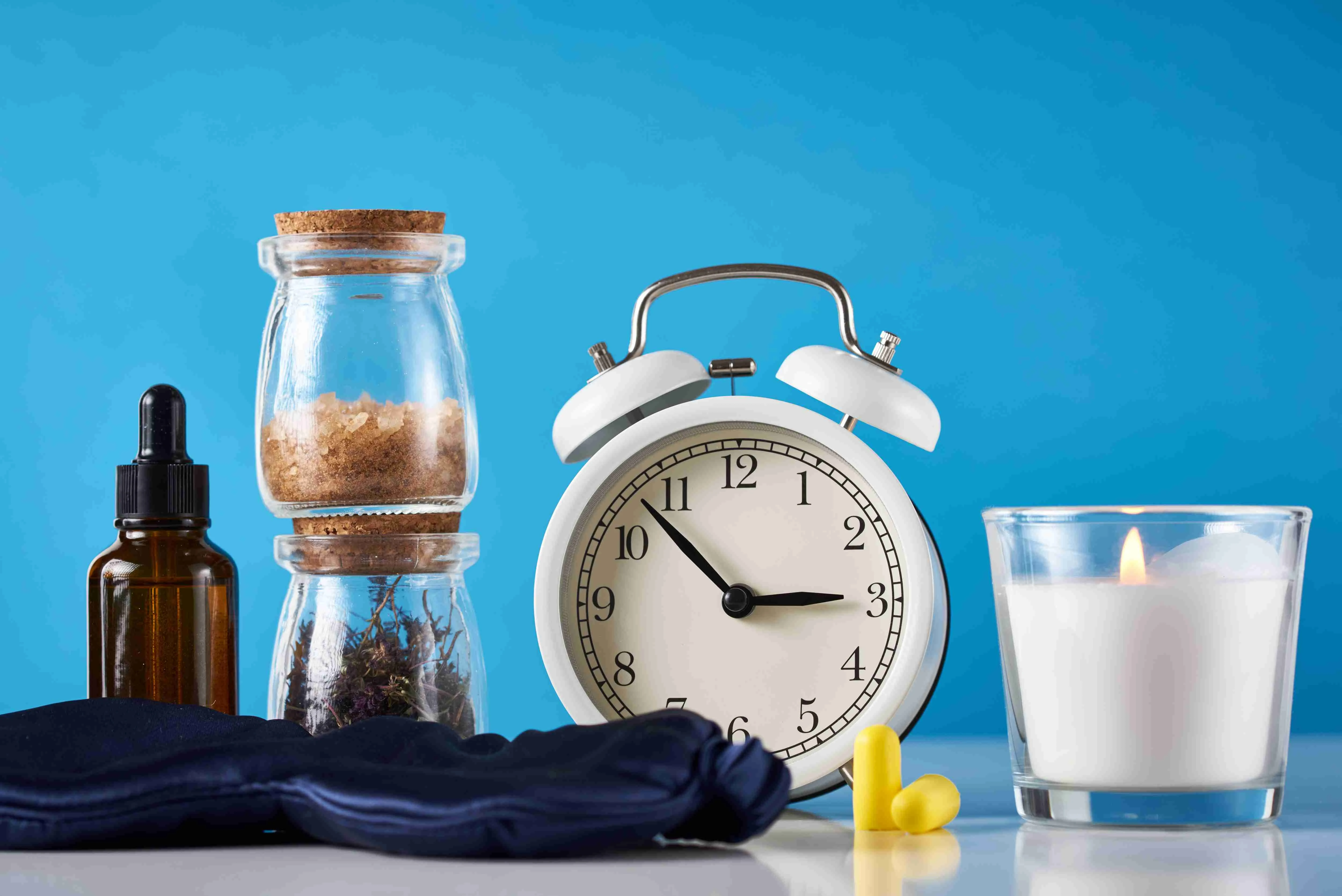 Herbal medicine for treat depression and insomnia concept. Alarm clock, medicine herbs and aromatherapy oil on blue background